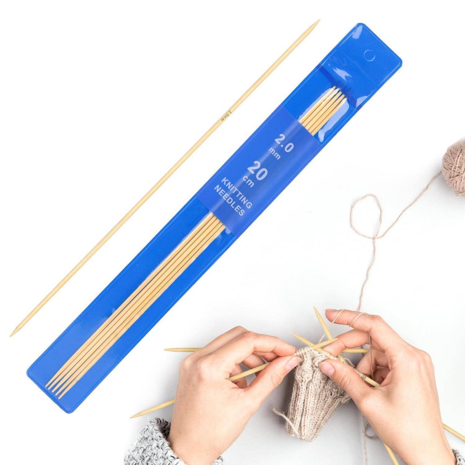 Hände, die mit Holzstricknadeln neben einer blauen 20-cm-Stricknadeltasche auf weißem Hintergrund stricken.