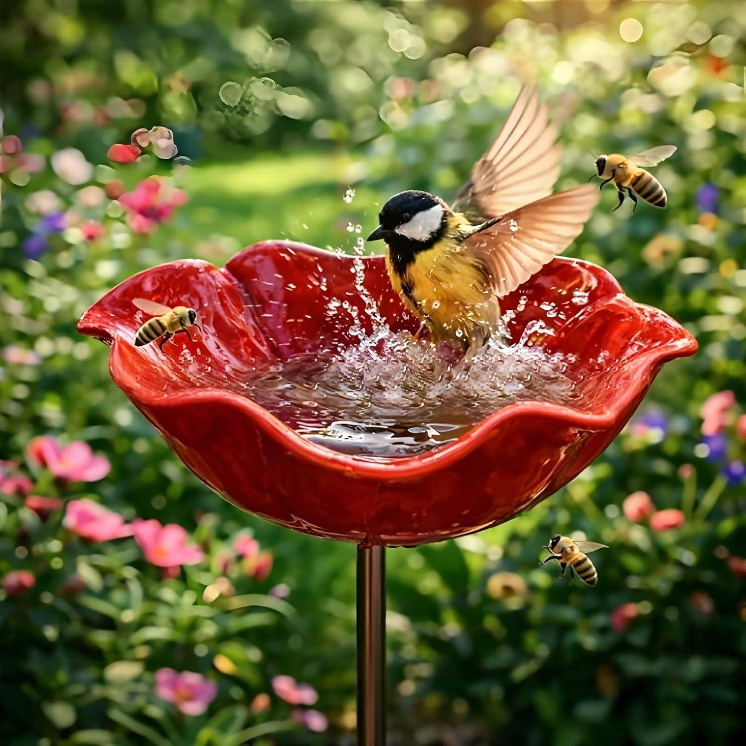 Ein kleiner Vogel planscht in einem roten, blütenförmigen Vogelbad, während Bienen in der Nähe in einem farbenfrohen Garten umherschwirren.