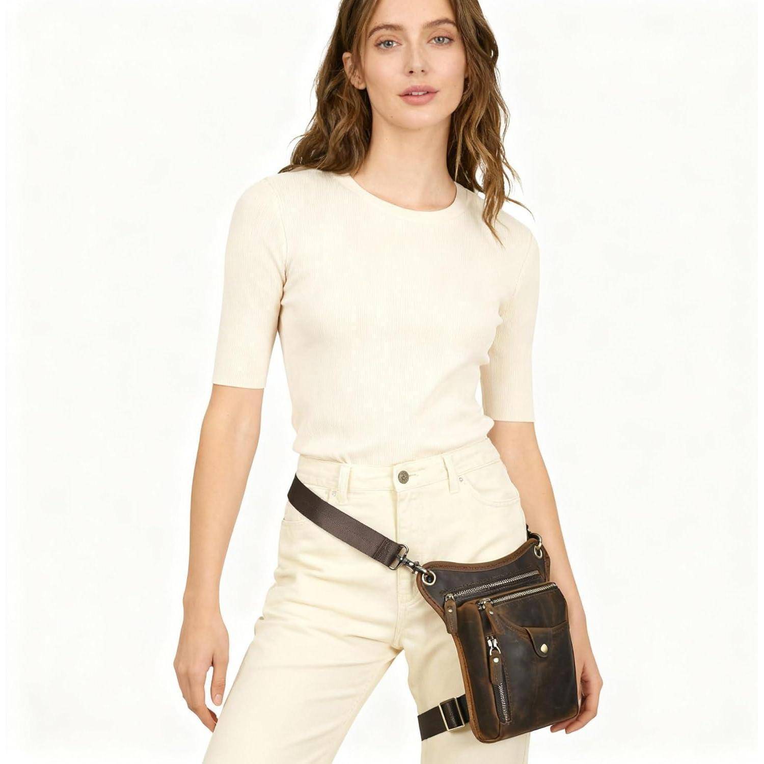 Frau, die ein elfenbeinfarbenes enganliegendes Oberteil und eine passende Hose mit einer dunklen Crossbody-Gürteltasche vor einem weißen Hintergrund trägt.