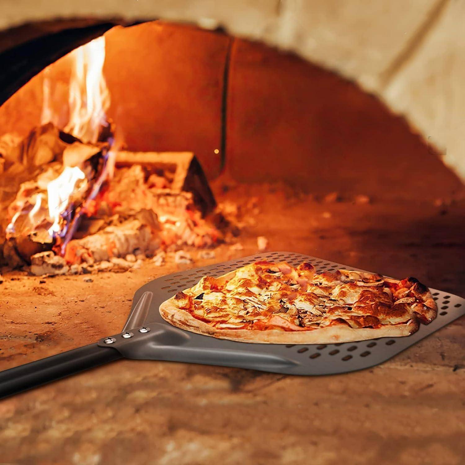 Pizza auf einer gelöcherten Pizzaschaufel wird aus einem holzbefeuerten Ofen entfernt, mit Flammen im Hintergrund.