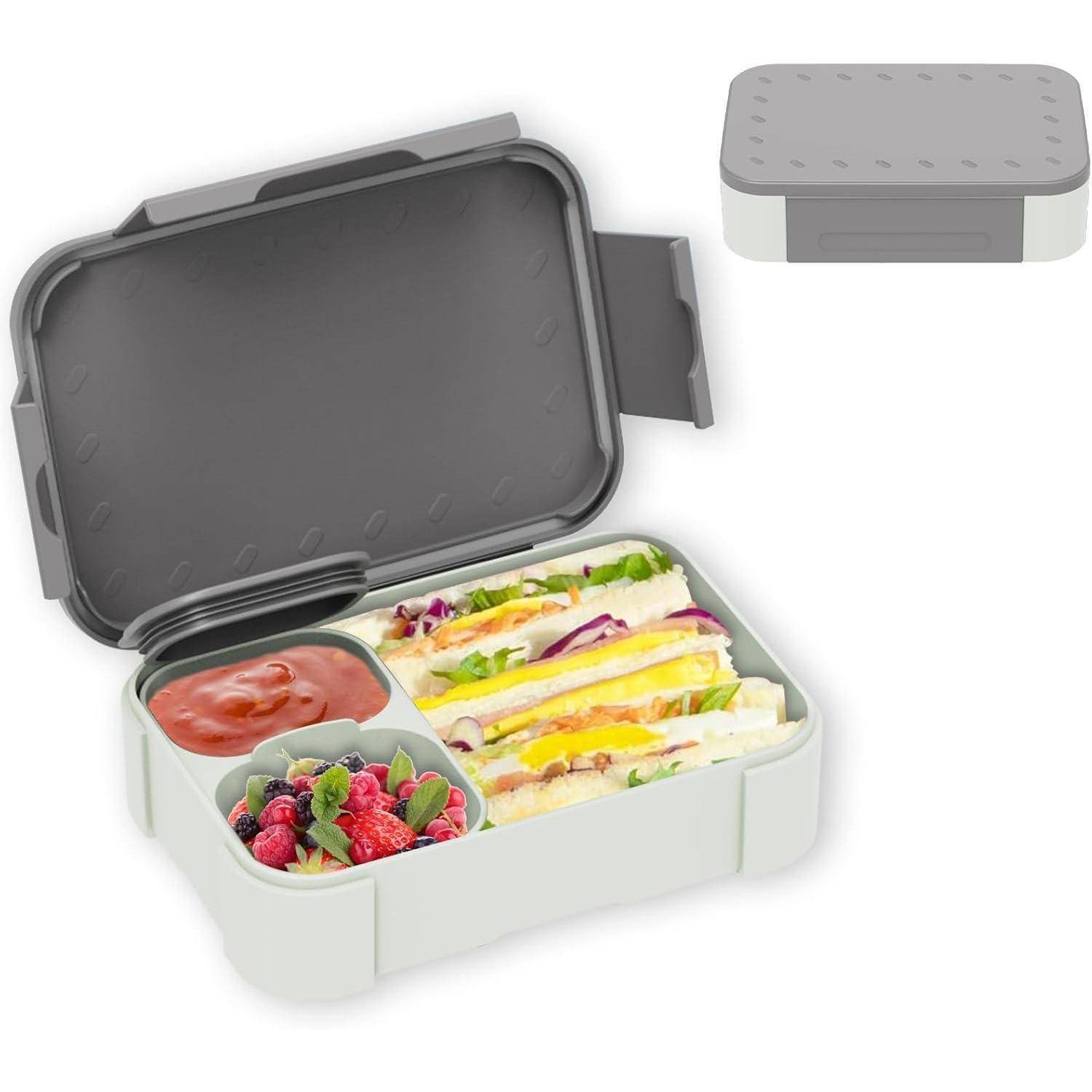 Offene graue Lunchbox mit abnehmbarem Deckel und Fächern, die Sandwich-Hälften, Soße und gemischte Beeren enthalten; kleiner geschlossener Behälter oben gezeigt.