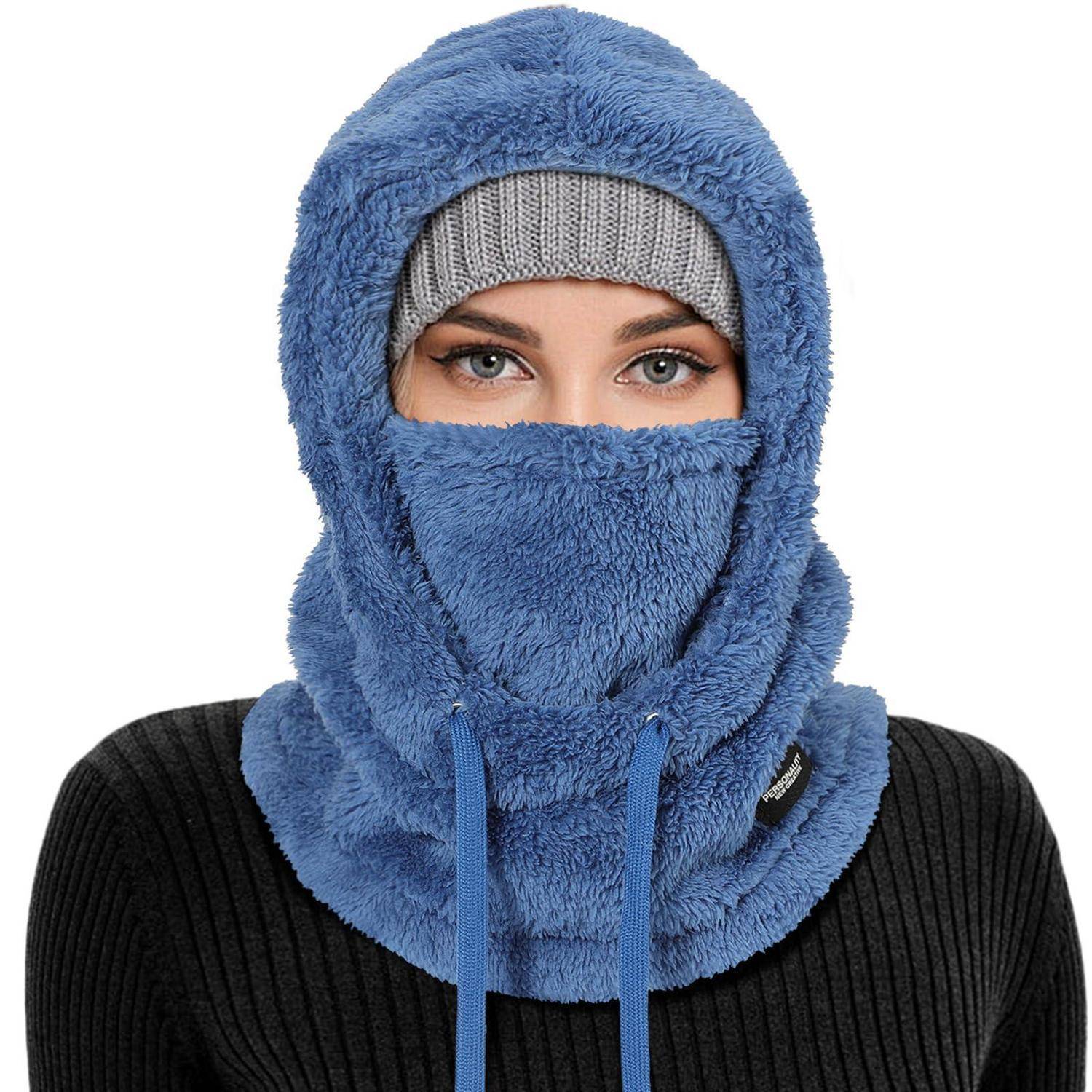 Frau, die eine blaue flauschige Sturmhaube im Balaclava-Stil und eine Gesichtsbedeckung trägt, wobei nur ihre Augen über einer grauen Strickmütze sichtbar sind.