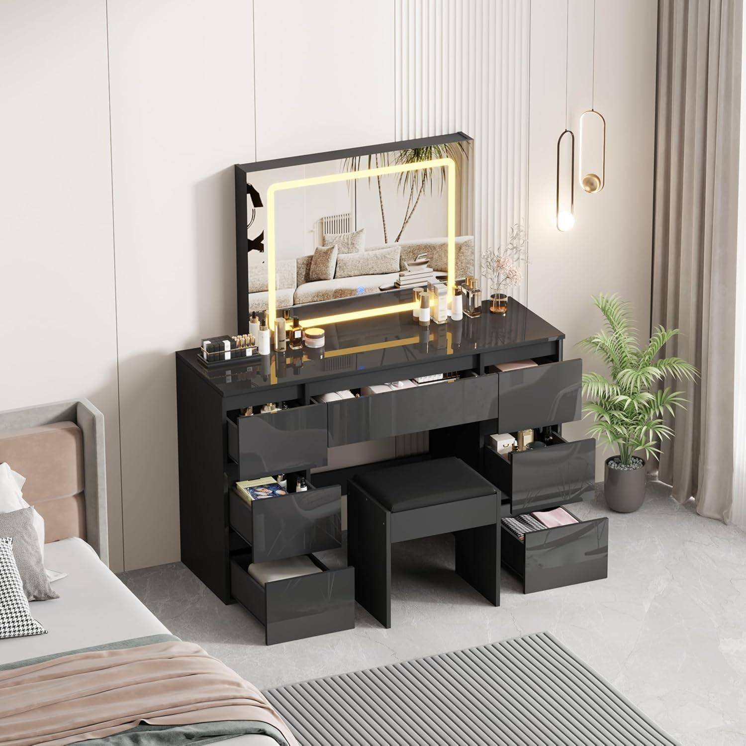 Schwarze Waschtischkommode mit beleuchtetem Spiegel, Schubladen und Hocker in einem modernen Schlafzimmer neben einem Bett, einer Pflanze und hängenden Pendelleuchten.