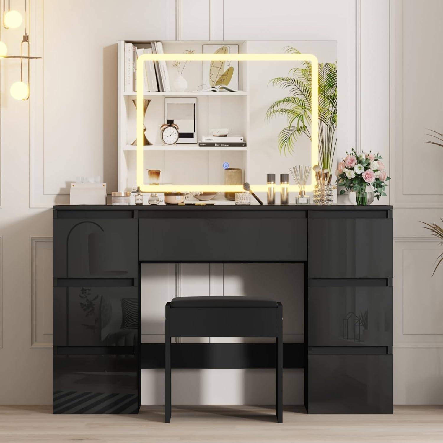 Schwarzer Frisiertisch mit beleuchtetem Spiegel, passendem Hocker, Regalen, Blumen und Dekorationen in einem hellen Zimmer.