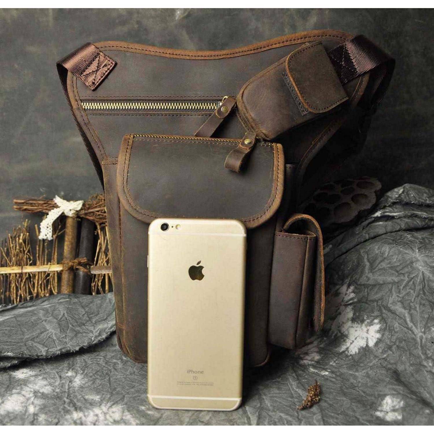 Braune Lederschulttertasche mit mehreren Taschen und Reißverschlüssen, mit einem goldenen iPhone davor zur Größenvergleich.
