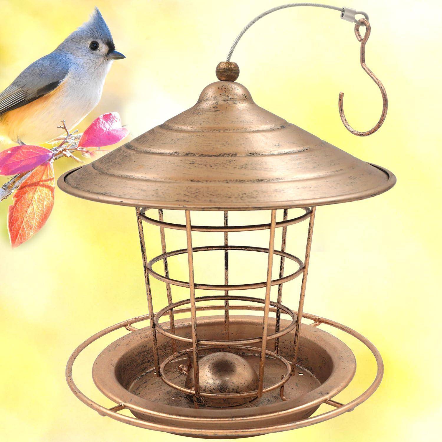 Blauer Vogel, der neben einem hängenden Metallvogelhaus mit Samenschale und Haken auf blassgelbem Hintergrund sitzt.