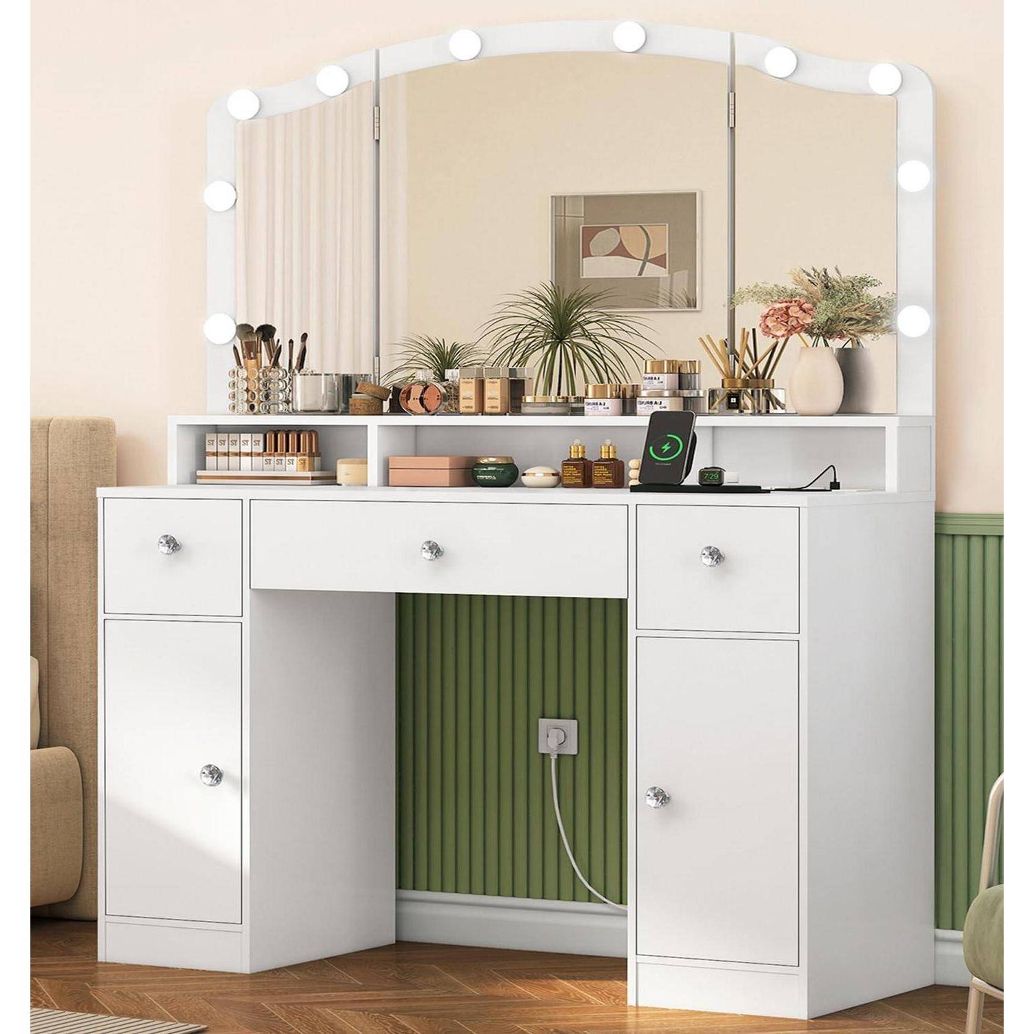 Weißer Frisiertisch mit Spiegellicht, Make-up und Toilettenartikeln sowie einem Ladegerät für das Telefon in einem ordentlichen Schlafzimmer oder Ankleidezimmer.