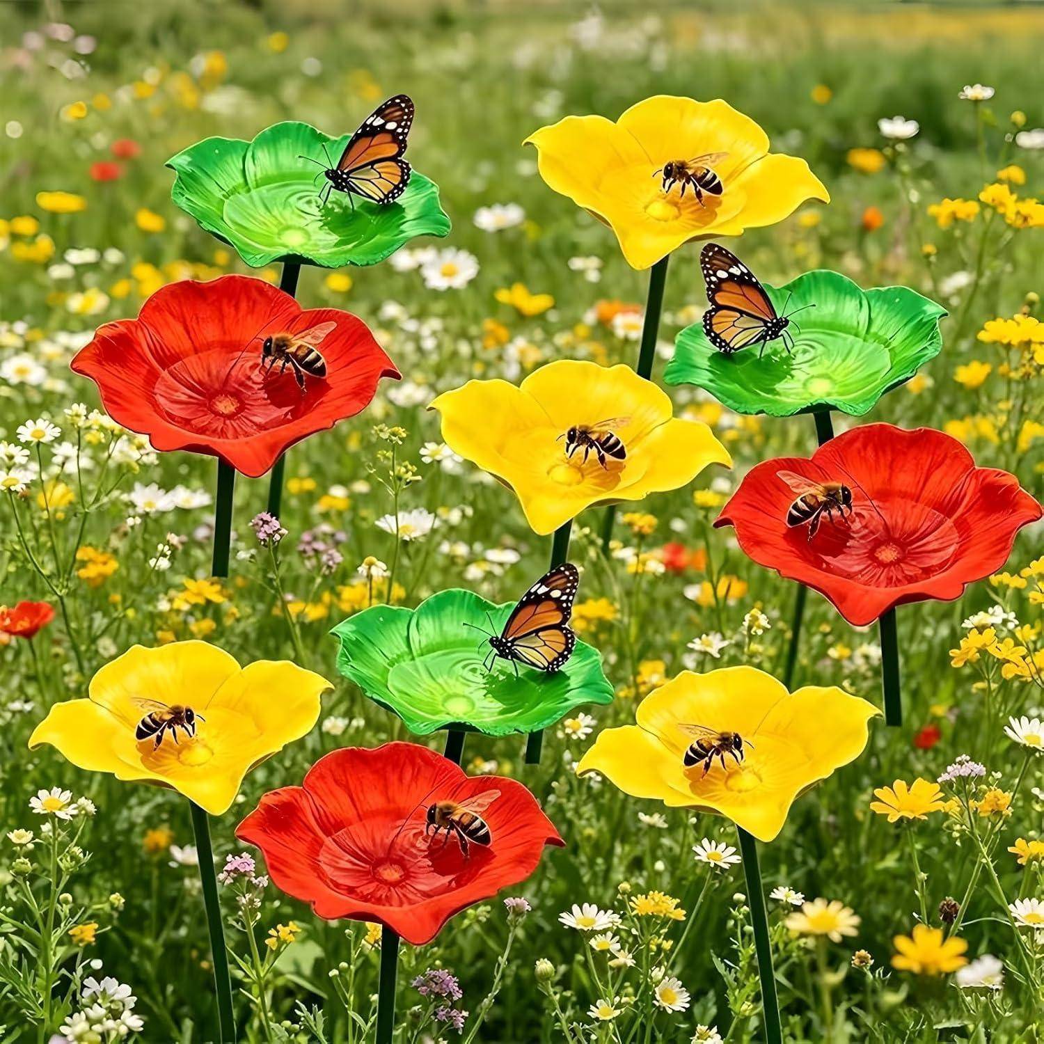 Schmetterlinge und Bienen sitzen auf farbenfrohen rot, gelb und grün gefärbten blumenförmigen Gartenstecken in einem grasigen Feld von Wildblumen.