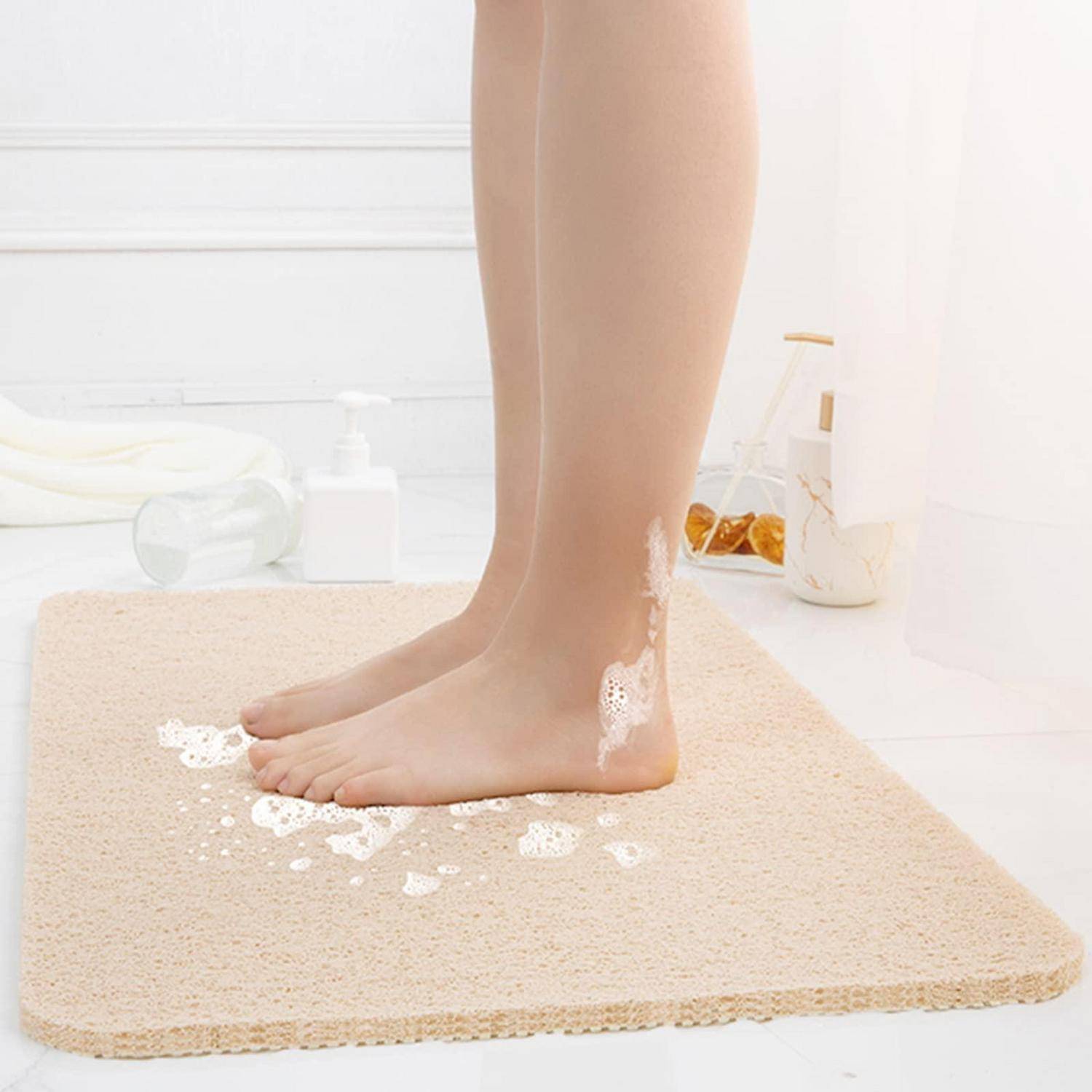 Nackte Füße stehen auf einer beigefarbenen Badmatte mit Seifenschaum, neben Badeutensilien in einem hellen Badezimmer.
