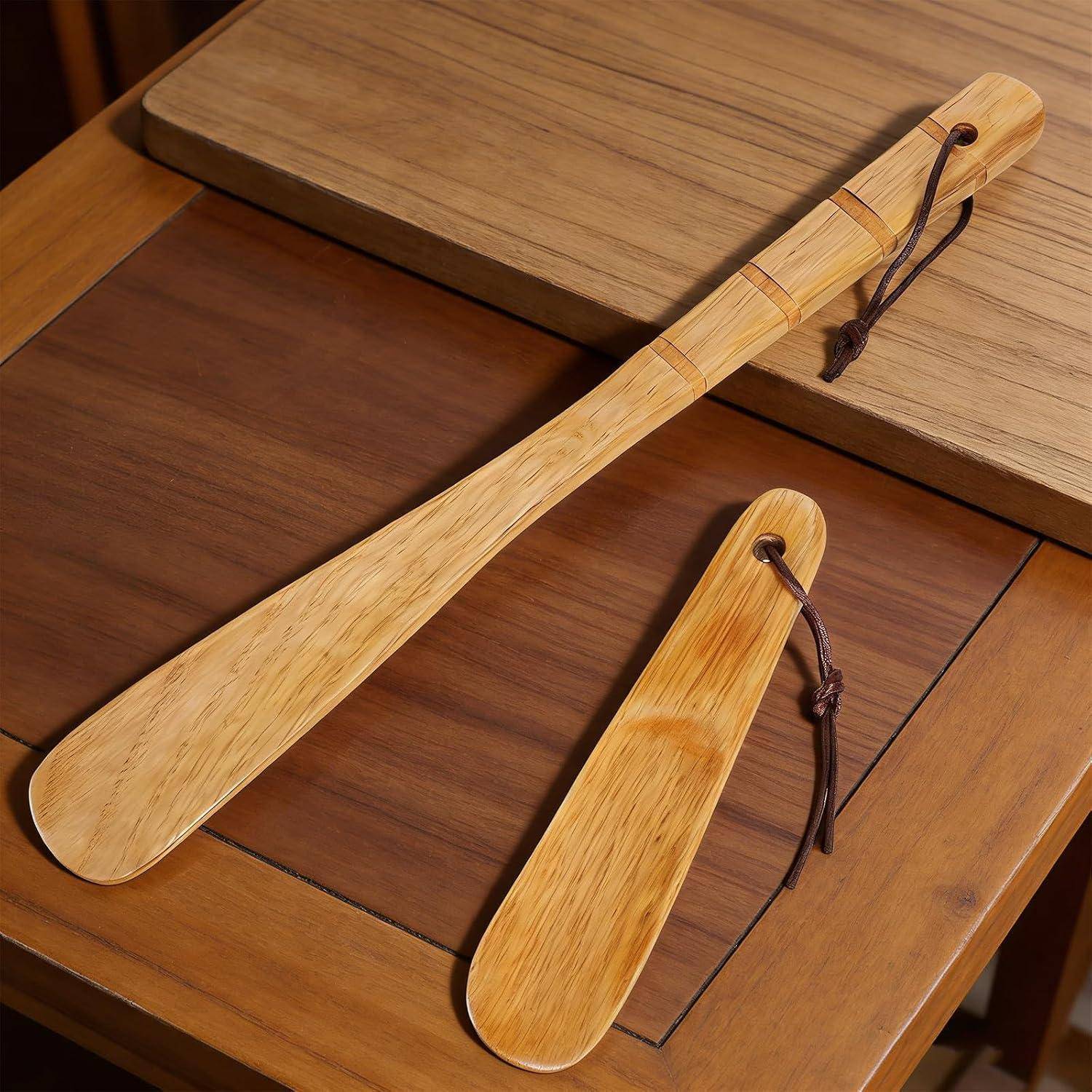 Zwei hölzerne Schuhlöffel mit Lederschnüren liegen auf einer Holztischplatte, einer lang und einer kurz.
