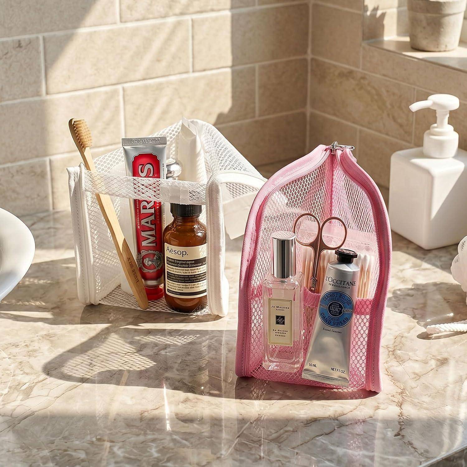 Zwei Netz-Toilettentaschen auf einem Badezimmertresen enthalten Reisegröße-Toilettenartikel, darunter Zahnpasta, Zahnbürsten, Parfüm und Lotion.