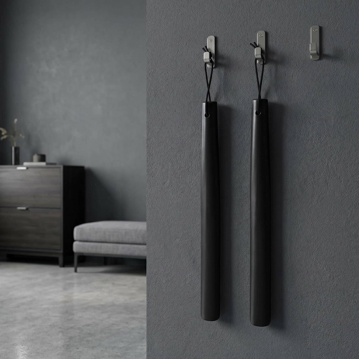 Zwei schwarze Regenschirmhalter hängen an einer grauen Wand in einem minimalistischen Eingangsbereich, mit einer Bank und einem Schrank im Hintergrund.