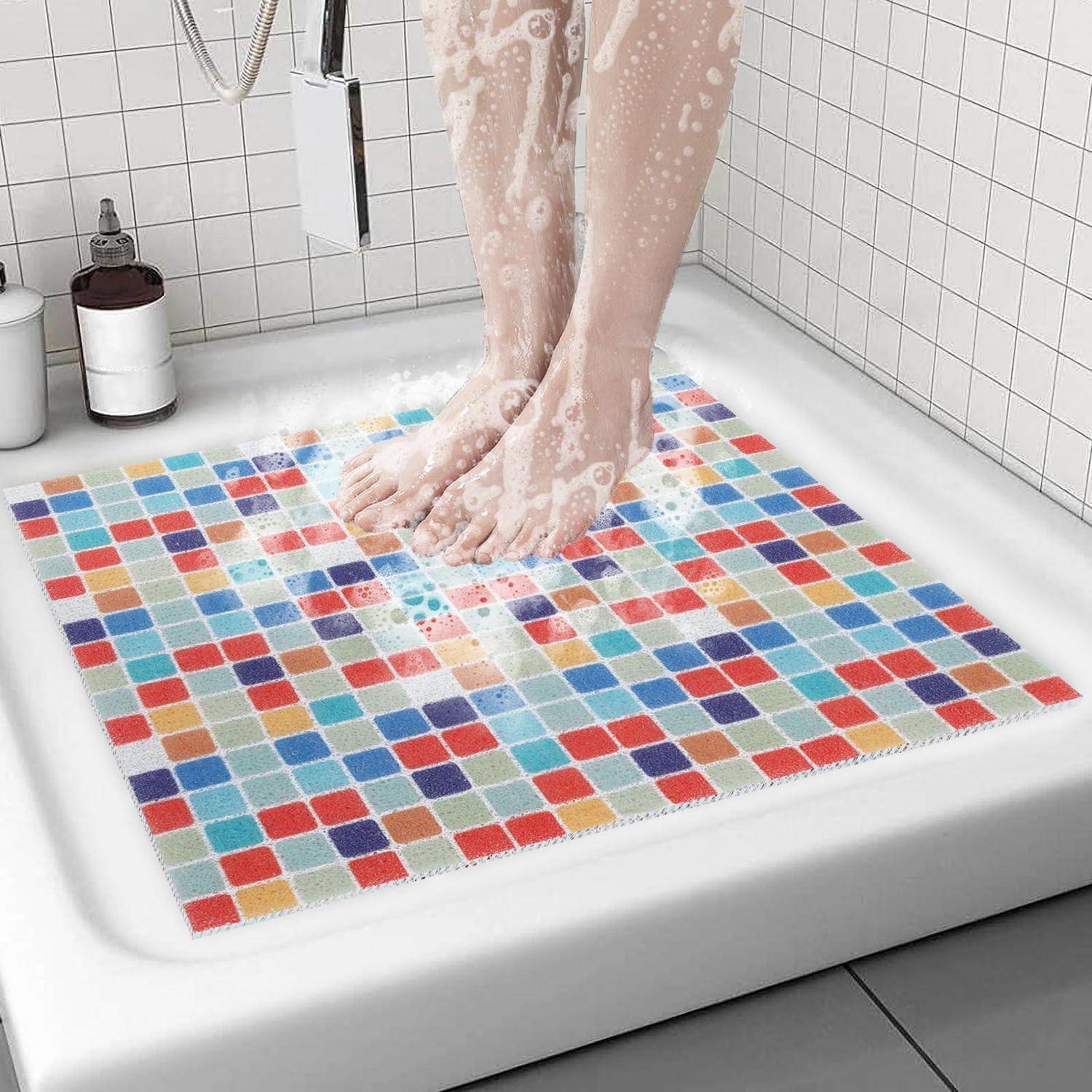 Füße duschen auf einer farbenfrohen quadratischen Mosaikbadeteppich in einer weiß gefliesten Dusche.