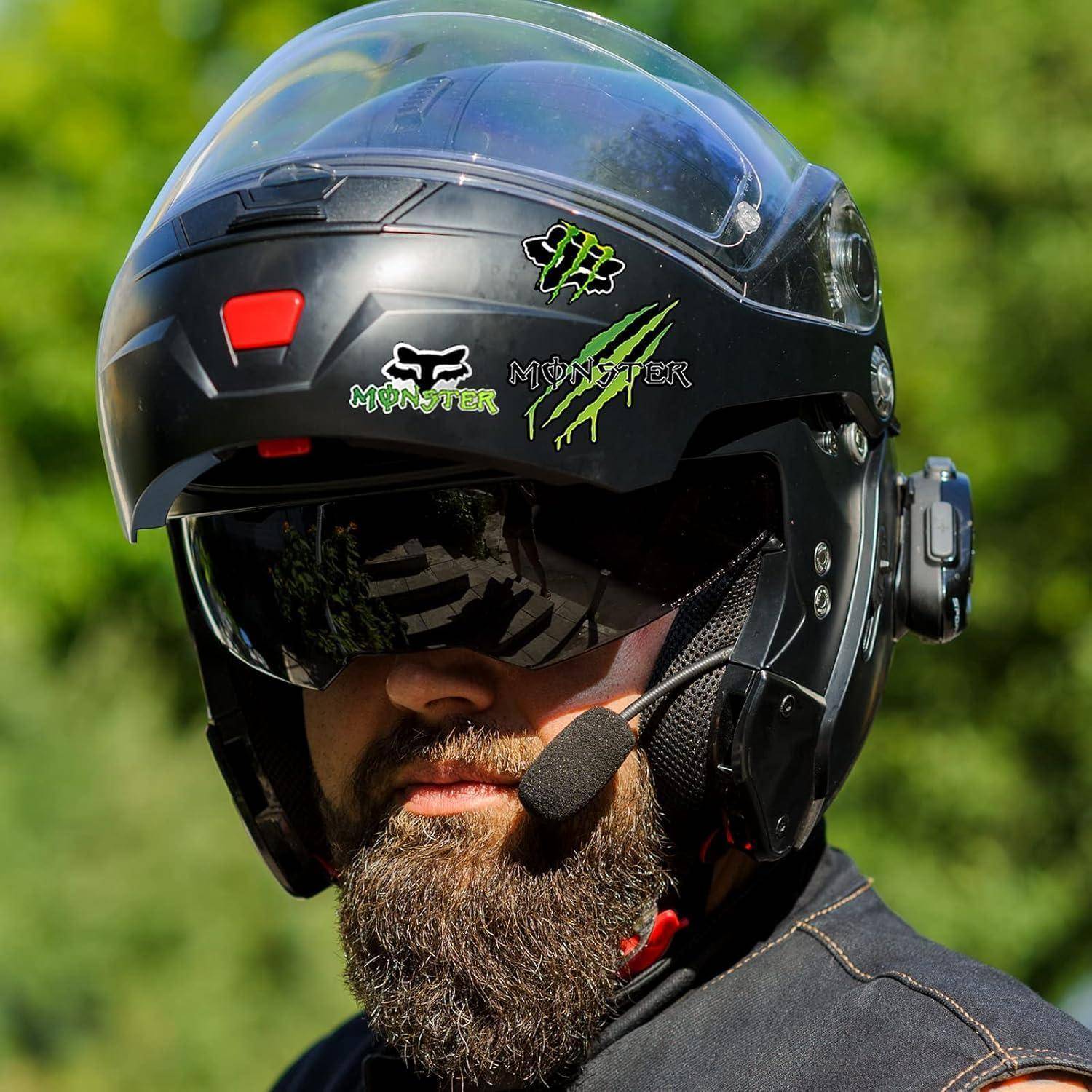 Nahaufnahme eines bärtigen Mannes, der einen schwarzen Motorradhelm mit Visier und Kopfhörer-Mikrofon trägt, draußen vor einem unscharfen grünen Hintergrund.
