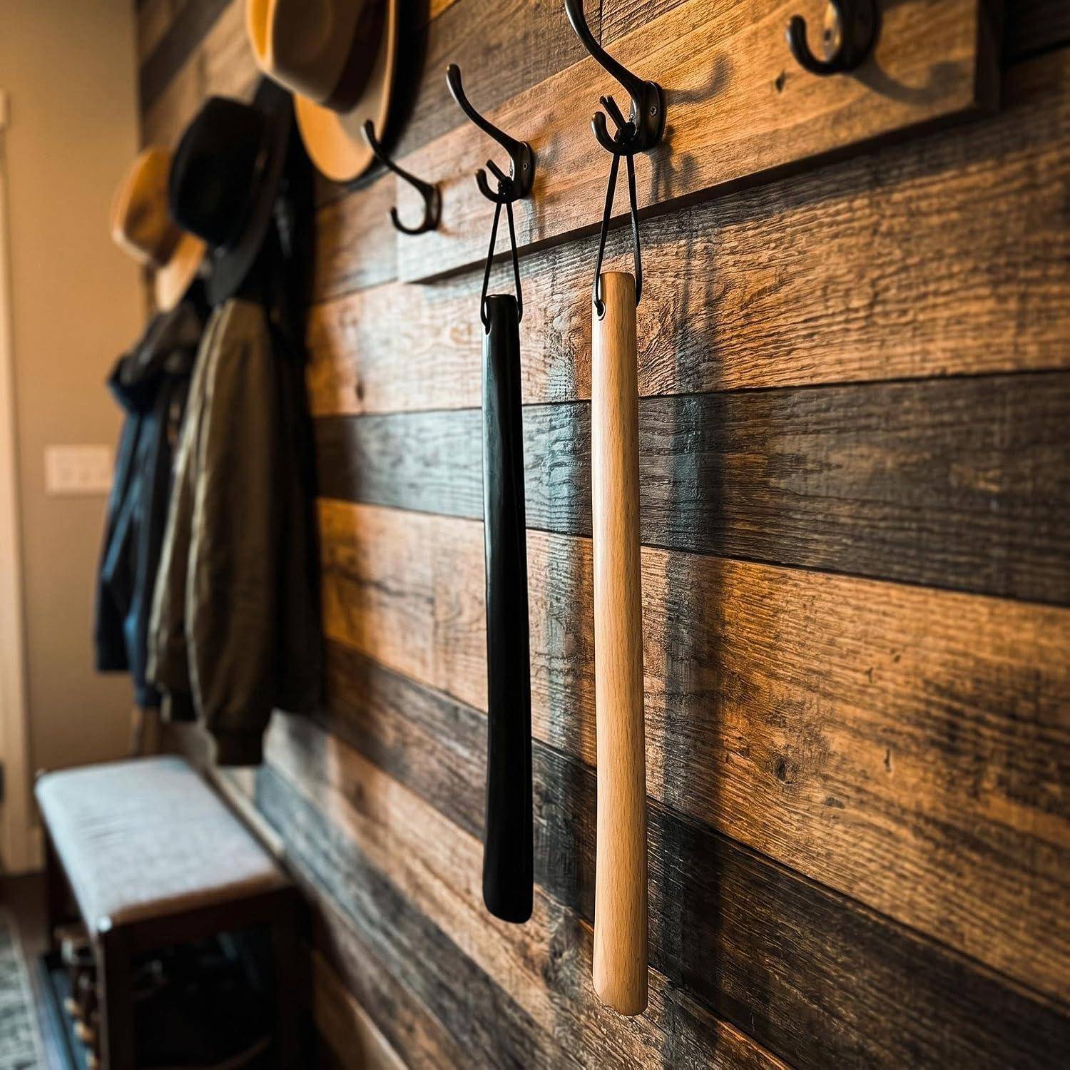 Holzwand mit Haken, an denen Hüte und Mäntel hängen, sowie zwei Stöcke/Stabspitzen, die in einem Flur oder Eingangsbereich hängen.