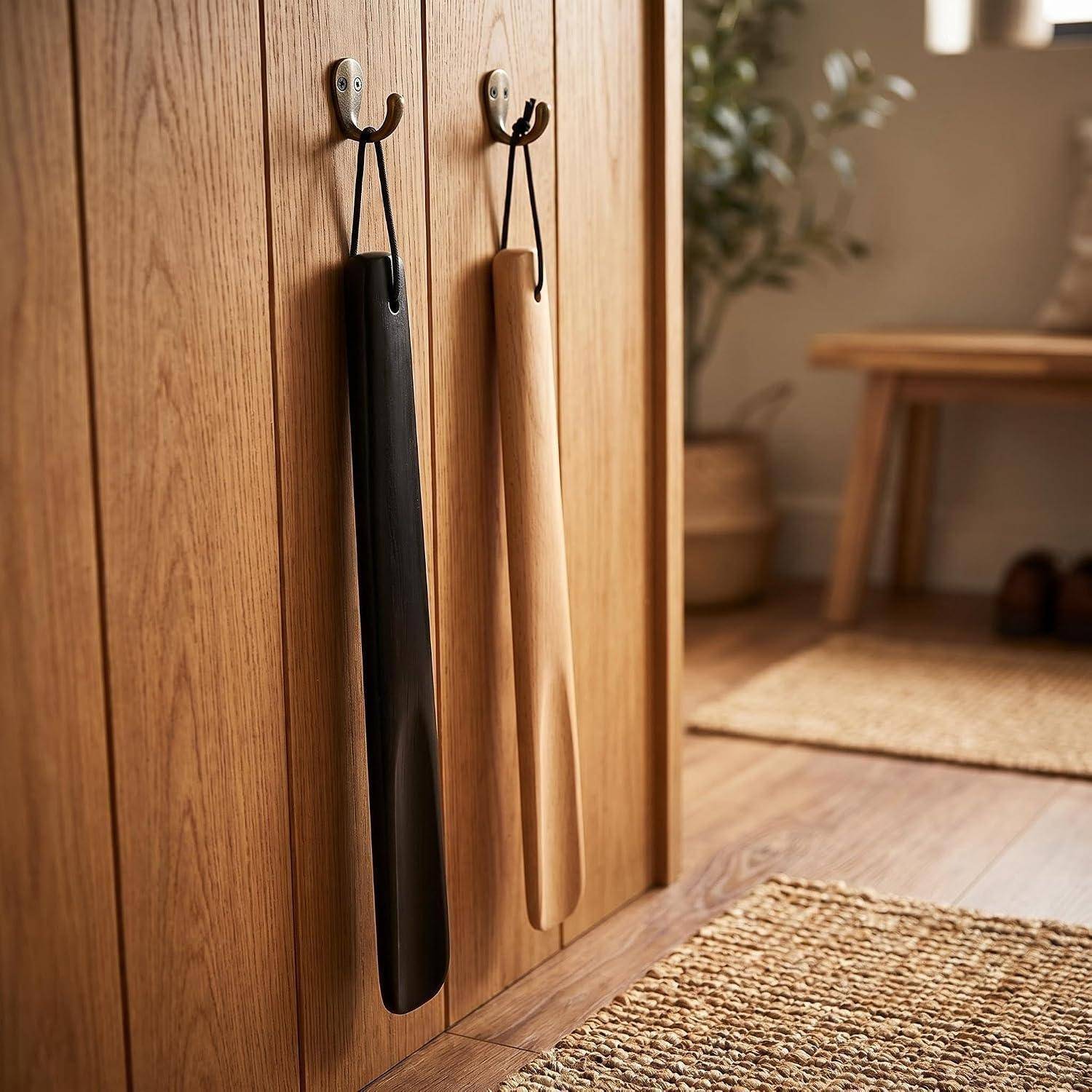 Zwei hölzerne Küchenutensilien hängen an Wandhaken neben einem Holzschrank in einem warm eingerichteten minimalistischen Raum.