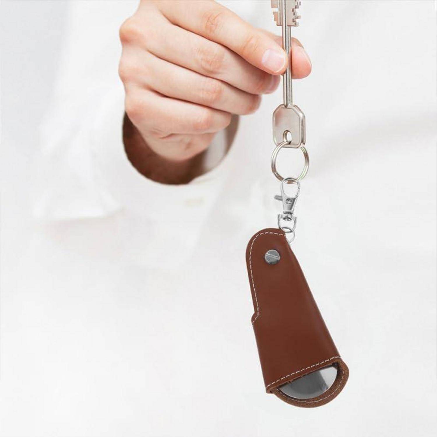Hand, die einen Schlüssel mit einem braunen Leder-Schlüsselanhänger an einem Ring hält, vor weißem Hintergrund.