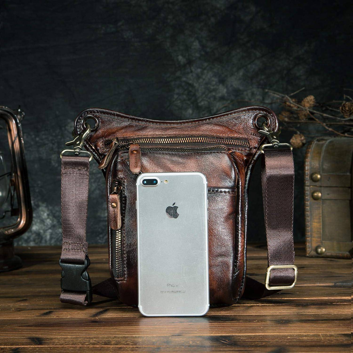 Braune Ledertasche zum Umhängen mit einem silbernen iPhone, das daran lehnt, auf einem Holztisch vor dunklem Hintergrund gezeigt.