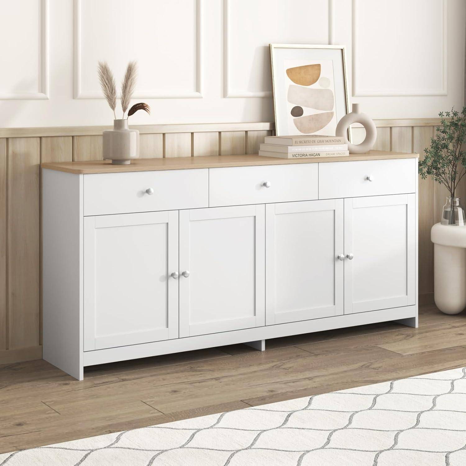 Weißer Sideboard-Schrank mit Holzplatte, dekoriert mit gerahmter Kunst, Büchern, Vase und Trockenblumen in einem hellen Wohnzimmer.