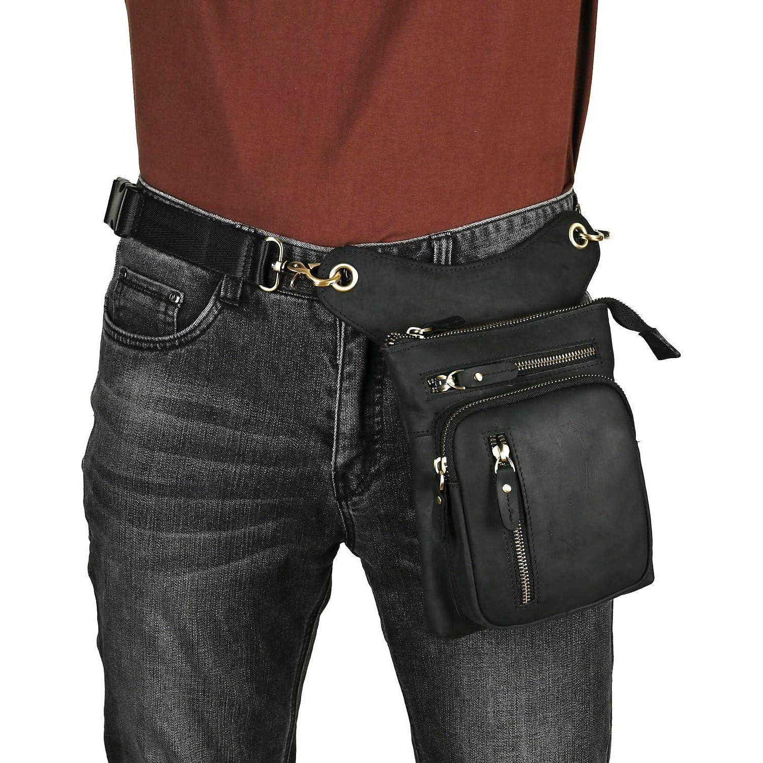 Person, die dunkle Jeans und eine schwarze Hüfttasche mit mehreren Reißverschlusstaschen trägt, die quer über den Hüften auf weißem Hintergrund getragen wird