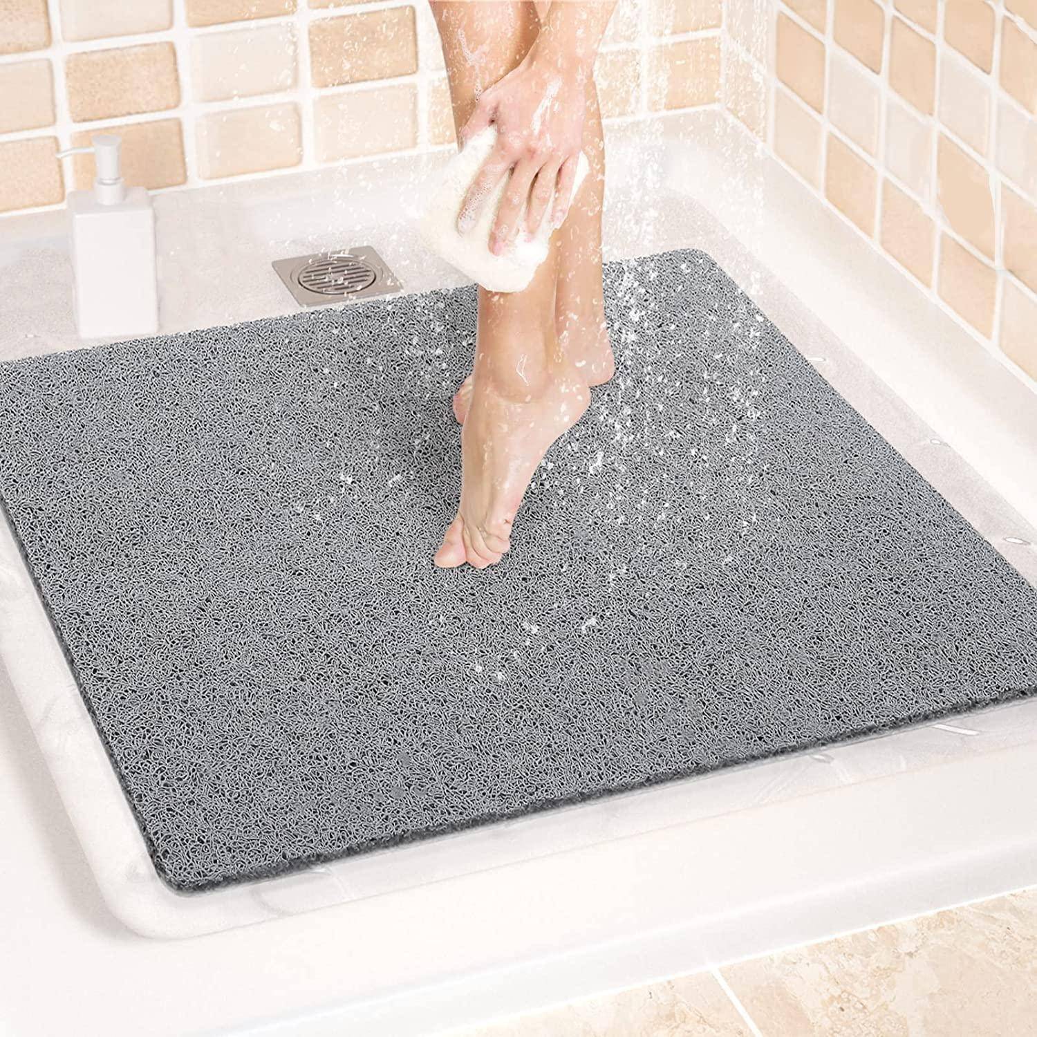 Eine Person wäscht sich unter der Dusche die Beine, während sie auf einer grauen rutschfesten Badewannenmatte steht.