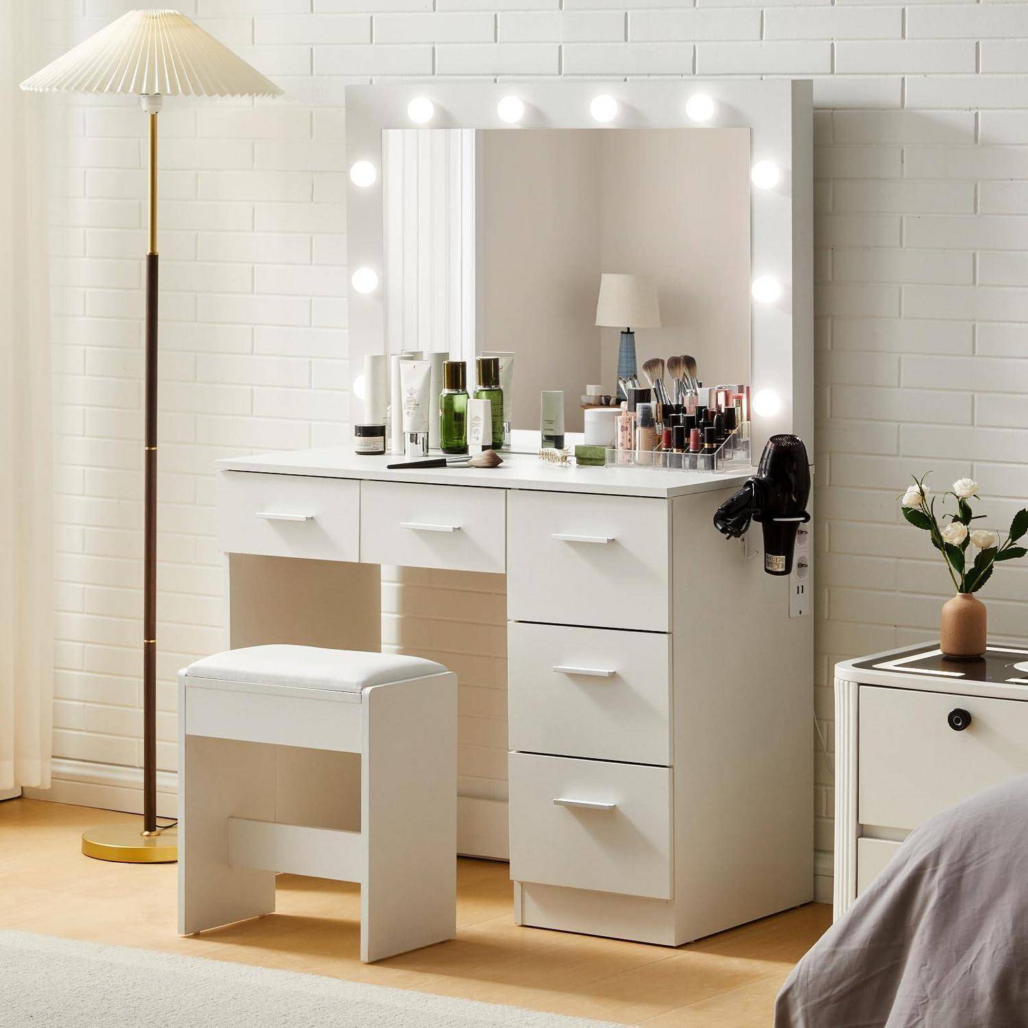 Weißer Frisiertisch mit beleuchteten Spiegel, Makeup-Artikeln, Hocker, Stehlampe und kleinem Schrank in einem hellen Schlafzimmer oder Ankleidezimmer.