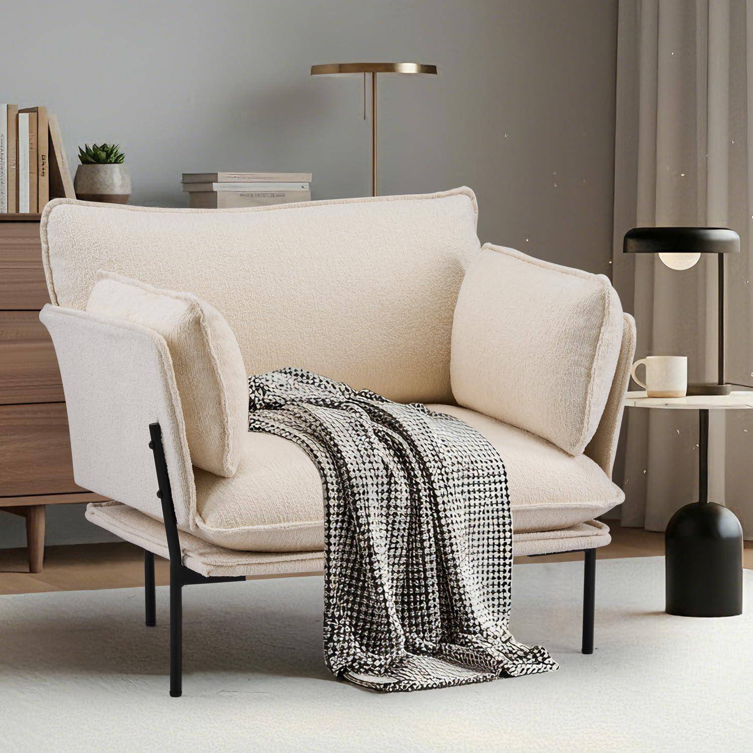 Creme-farbener Polstersessel mit schwarzem Metallrahmen, mit einer drapierten schwarz-weißen Decke, in einem modernen Wohnzimmer neben einem Beistelltisch und einer Lampe.