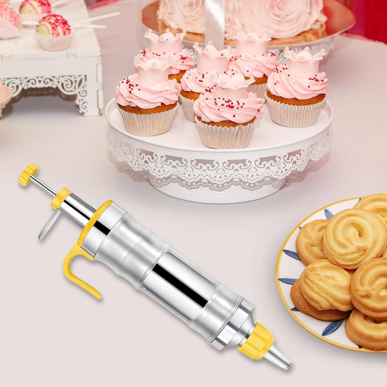 Metallische Plätzchenspritze mit gelben Akzenten, die neben Cupcakes und Keksen auf einem Dessert-Tisch präsentiert wird.
