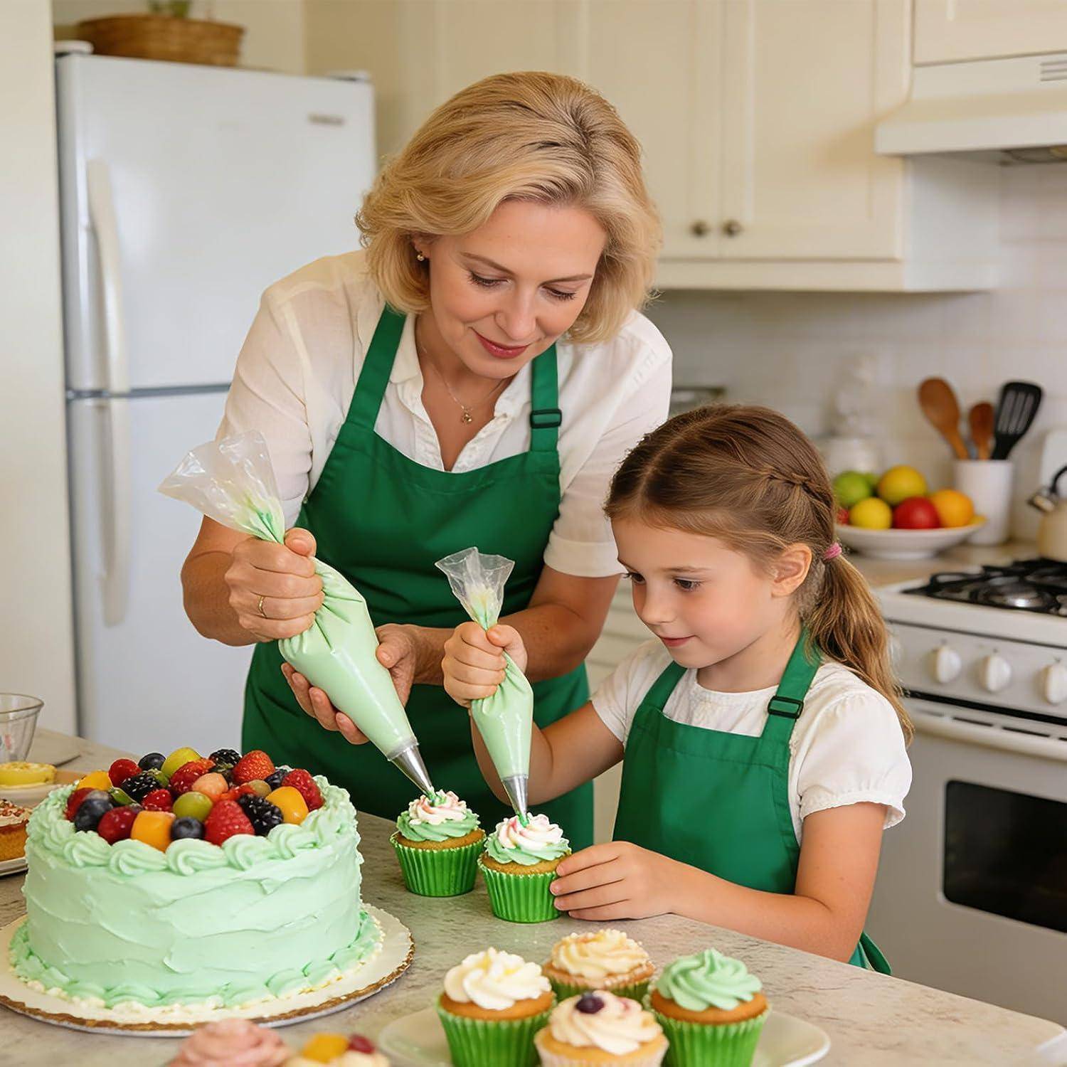 Eine Frau und ein junges Mädchen in Schürzen spritzen Zuckerguss auf Cupcakes in einer Küche neben einem dekorierten Kuchen und einer Schale mit Obst.