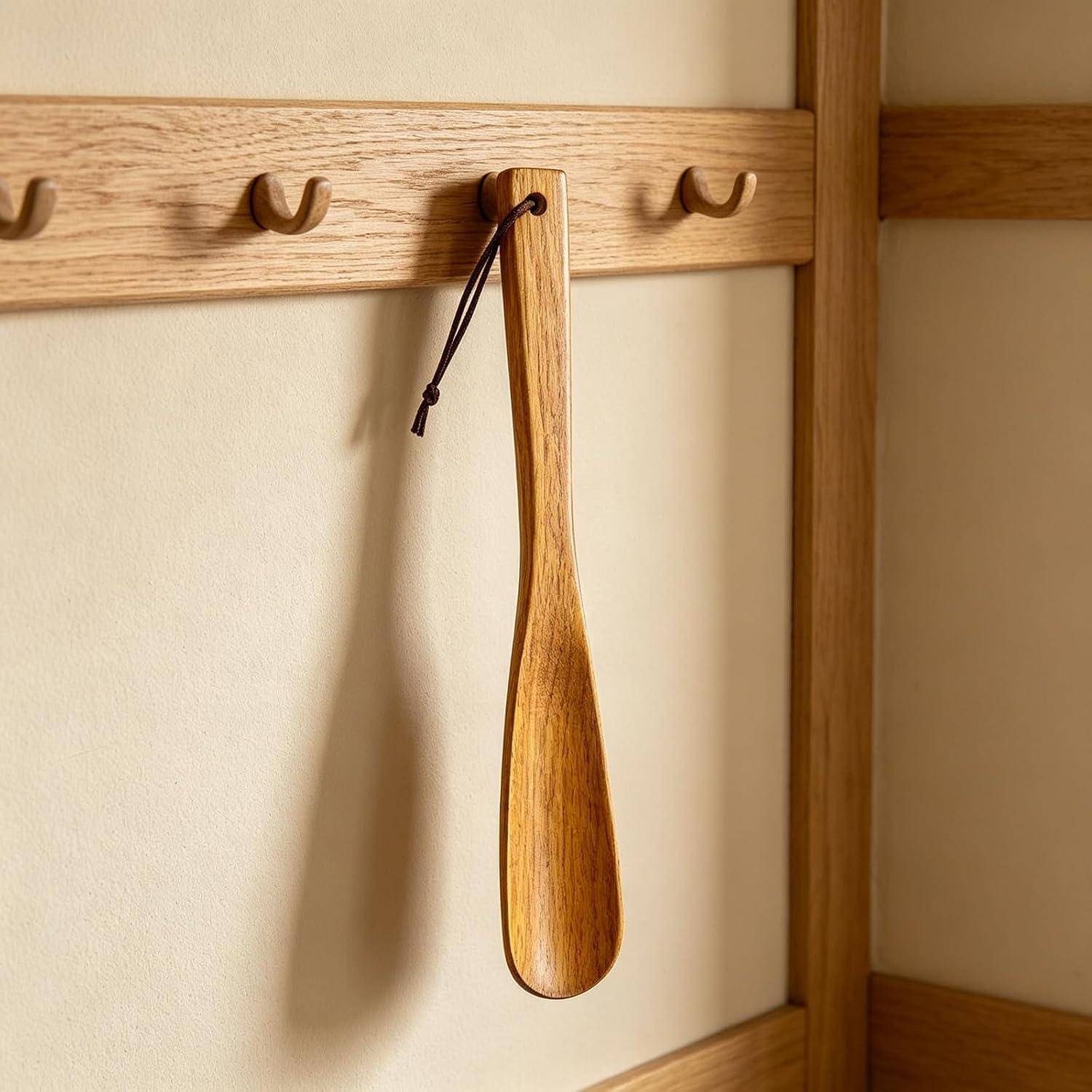 Holzerner Schuhlöffel zum Aufhängen an einem wandmontierten Eichenpflockregal an einer schlichten beigen Wand.