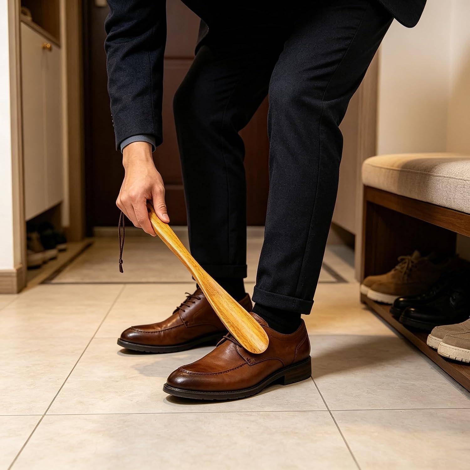 Ein Mann in Anzughosen und braunen Schuhen benutzt einen Schuhlöffel aus Holz, während er einen Schuh in einem Kleiderschrank oder Eingangsbereich anzieht.