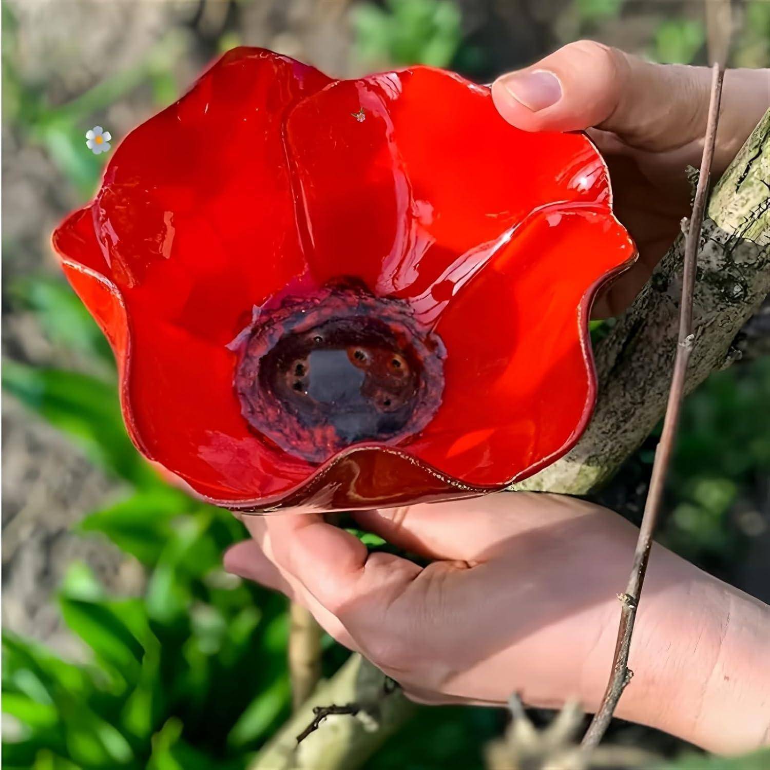 Hände halten eine rote Glasschale in Blütenform oder einen Kerzenhalter draußen gegen einen Baum und grünes Laub.