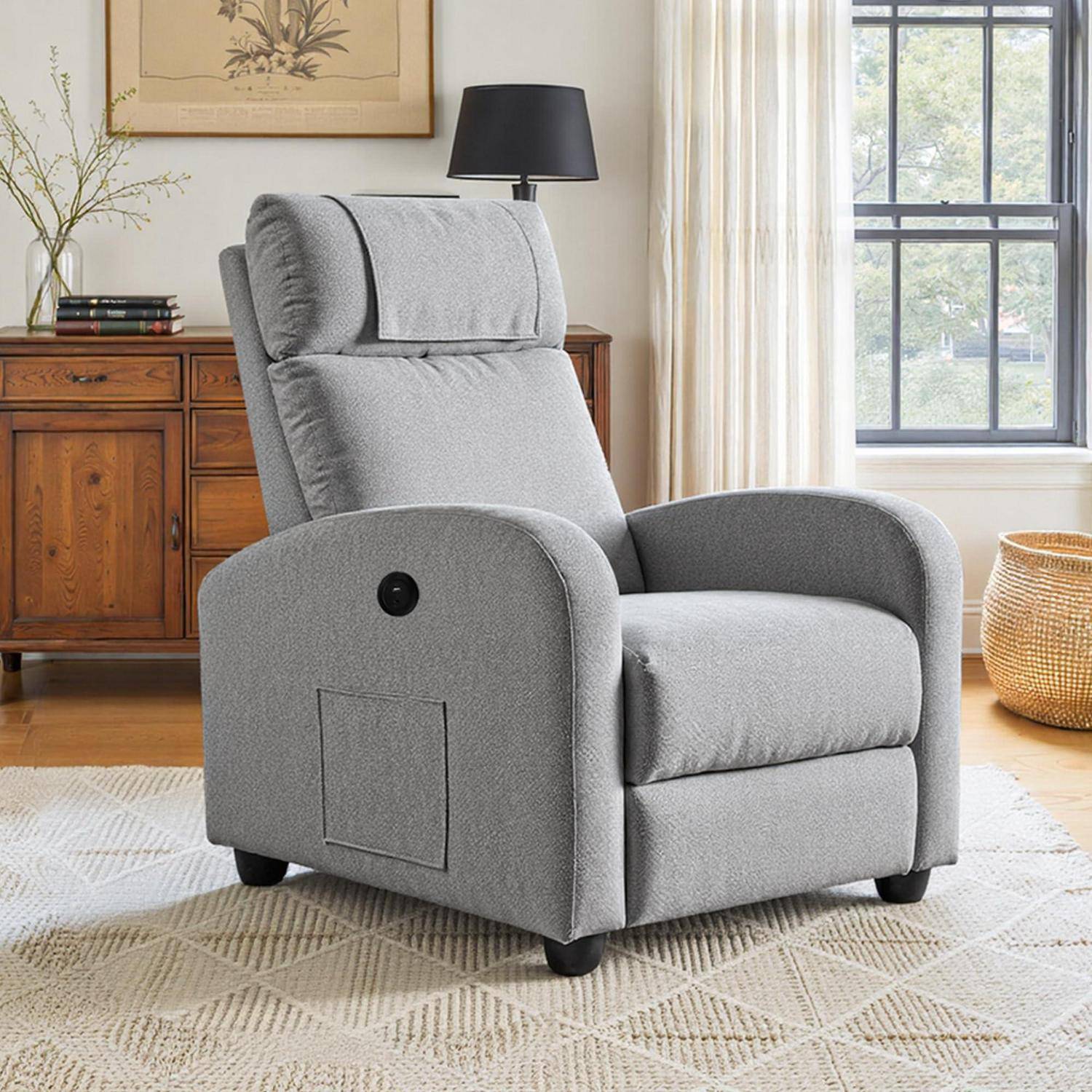 Grauer gepolsterter Relaxsessel in einem hellen Wohnzimmer, aus einem Winkel gezeigt mit gepolsterter Kopfstütze, Armlehnen und zurückgelehnter Rückenlehne.