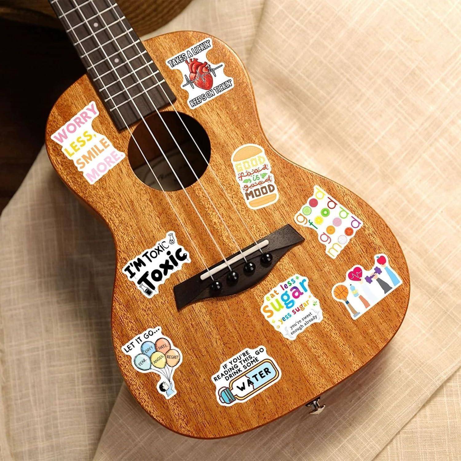 Holz-Ukulele mit bunten motivierenden Aufklebern dekoriert, liegt auf einer beigen strukturierten Stoffoberfläche.