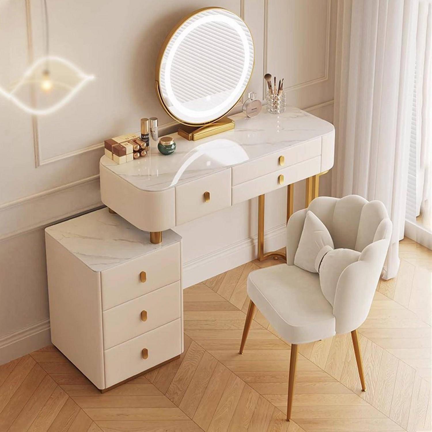 Moderner Waschtisch mit beleuchtetem rundem Spiegel, weißen Schubladen und goldenen Akzenten neben einem beige gepolsterten Stuhl in einem hellen Raum.