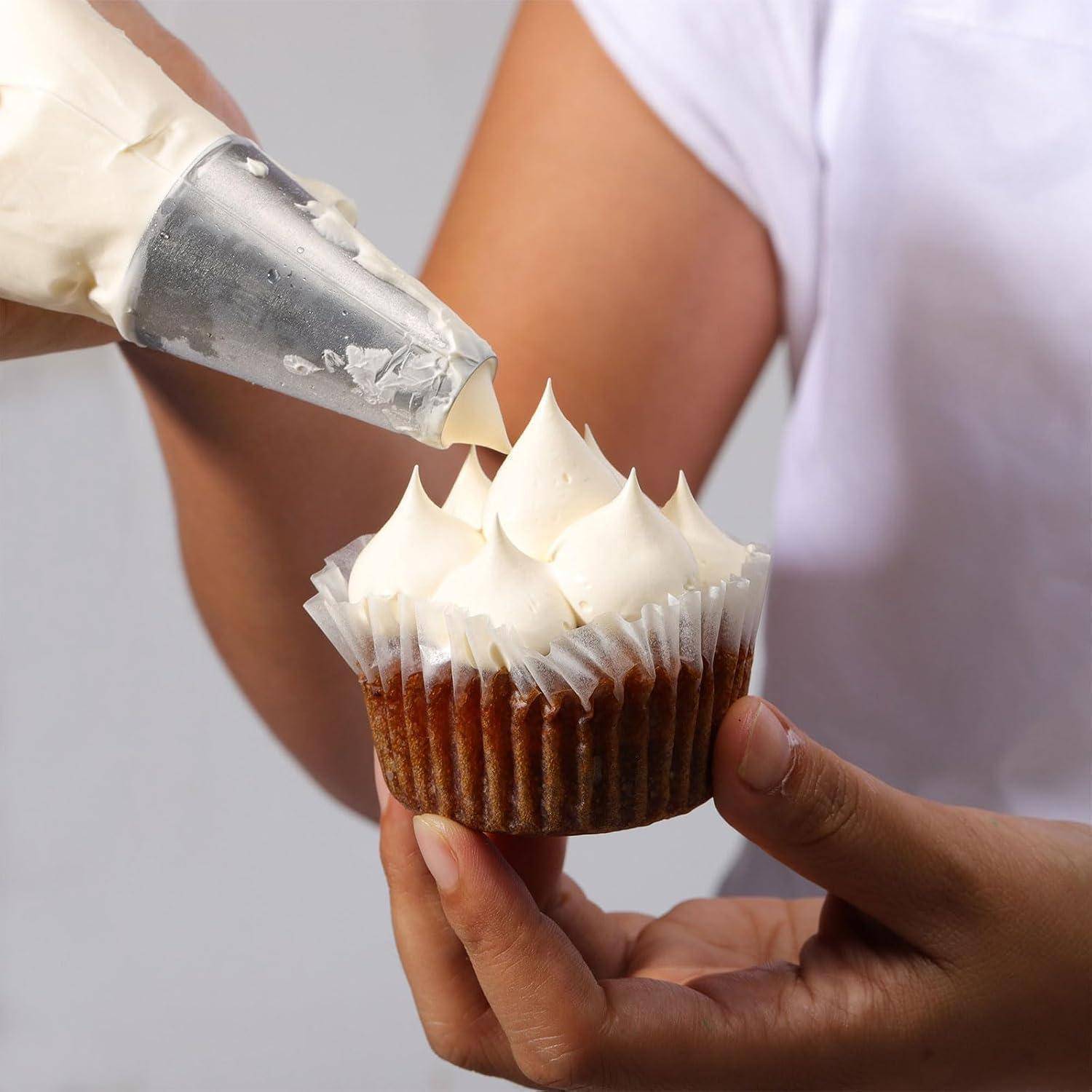 Eine Person spritzt weiße Glasur mit einer Spritztüte auf einen Cupcake, den sie in einer Hand hält, und verziert ihn damit.