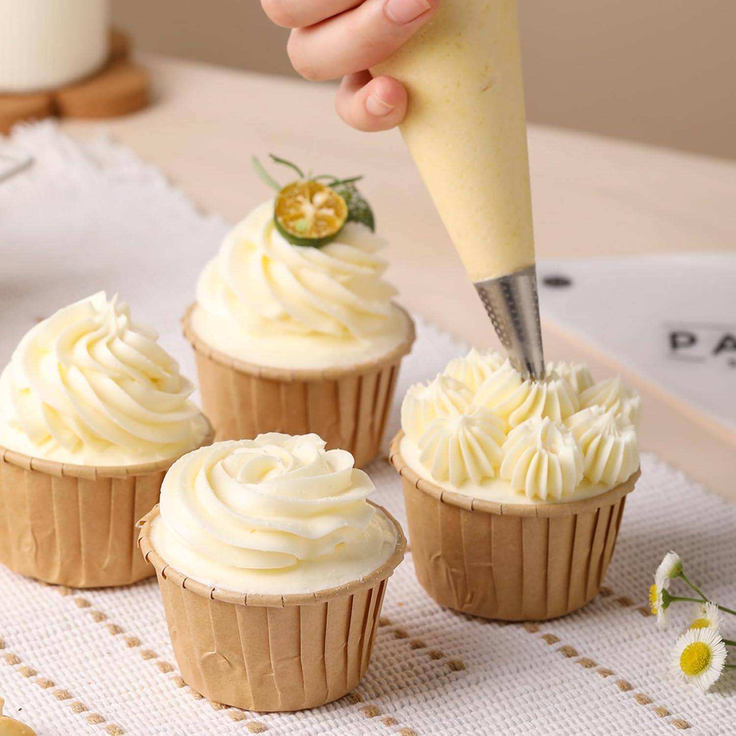 Mit der Hand wird weiße Glasur auf einen Cupcake gepresst, der sich unter vier Cupcakes in Papierförmchen auf einem Tisch befindet, einer davon ist mit einer kleinen Zitronendekoration belegt.