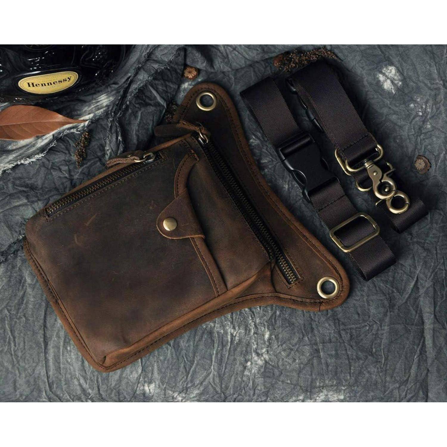 Braune Ledertasche zum Umhängen mit Messingreißverschluss und zwei schwarzen verstellbaren Riemen, präsentiert auf einem strukturierten dunklen Stoffhintergrund.