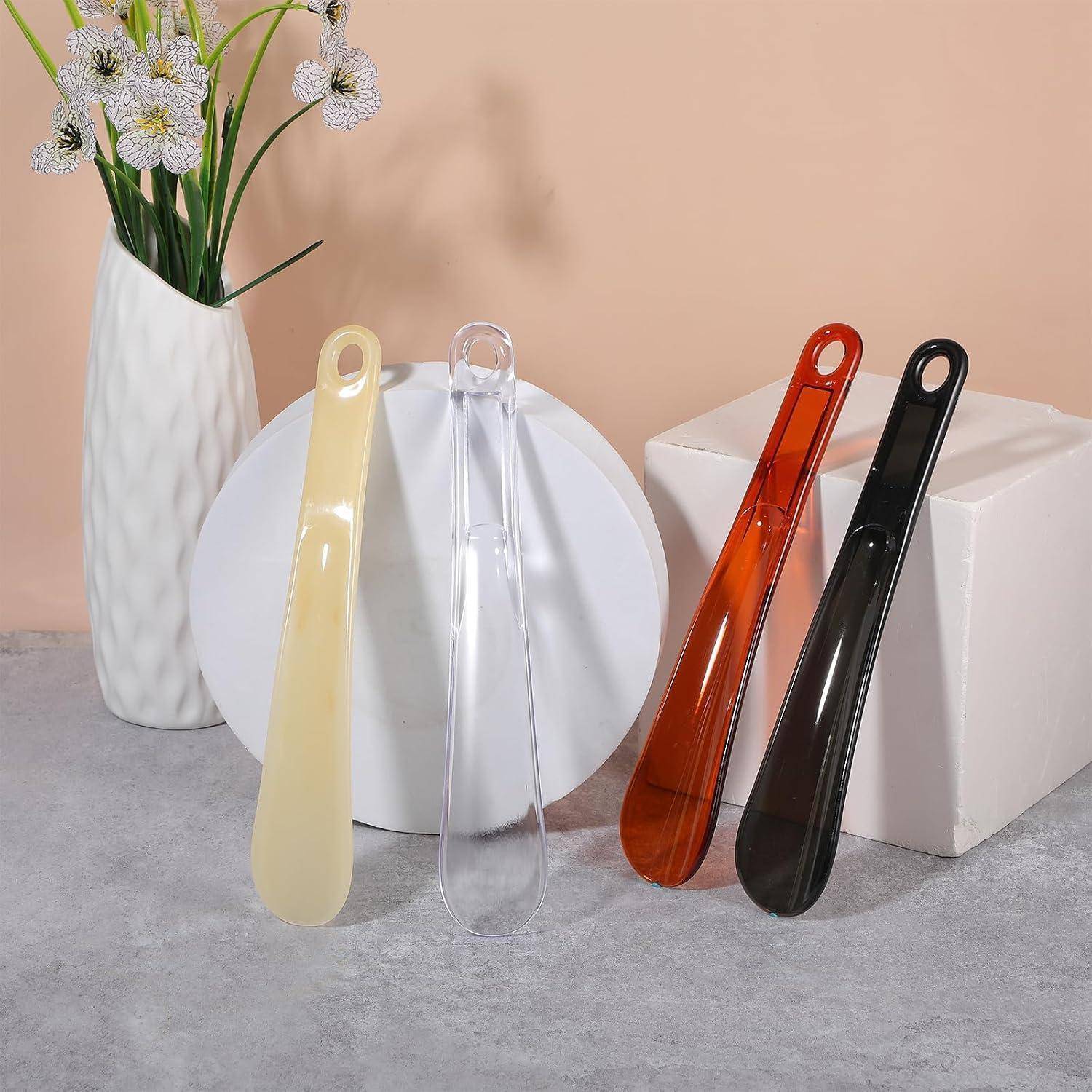 Fünf durchscheinende Kunststoff-Schuhanziher in Beige, Transparent, Orange und Schwarz arrangiert mit einem weißen Teller, einer Blumenvase und weißem Blockkarton-Hintergrund.