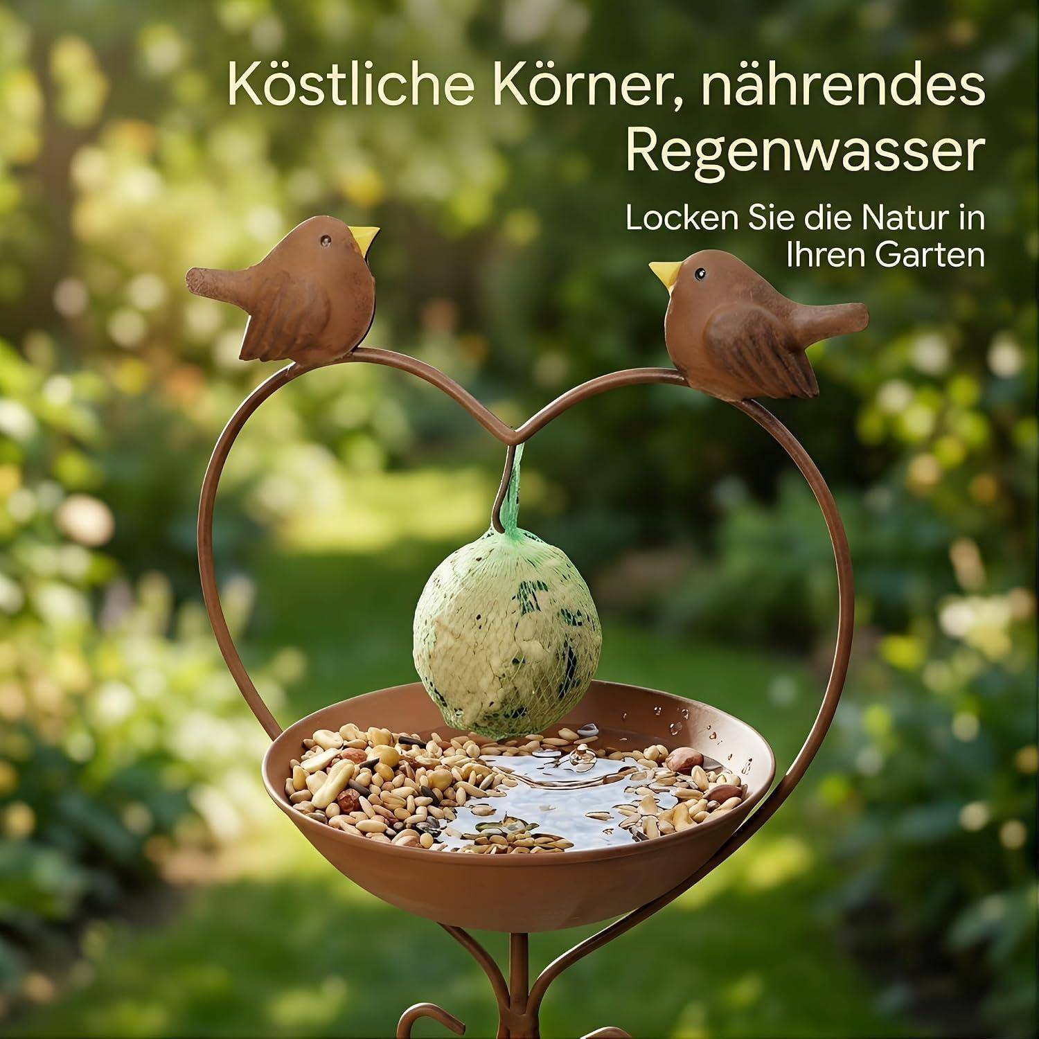 Futterhaus für Gartenvögel in Herzform mit zwei Vogelfiguren, das Samen und Wasser hält; deutscher Text sagt „Köstliche Körner, nährendes Regenwasser" und „Locken Sie die Natur in Ihren Garten"".