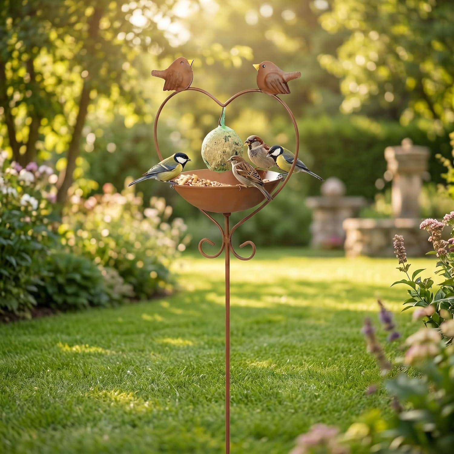 Vier kleine Vögel saßen auf einem herzförmigen Gartenfutterhaus und pickten im sonnigen Hinterhof nach Futter.