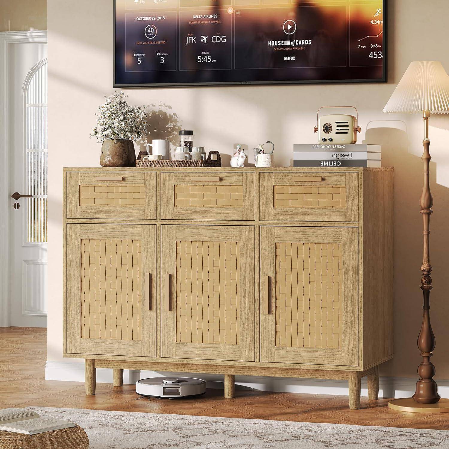 Ein hölzernes Sideboard mit Deko, eine Stehlampe und ein an der Wand montierter Fernseher in einem hellen Wohnzimmer.