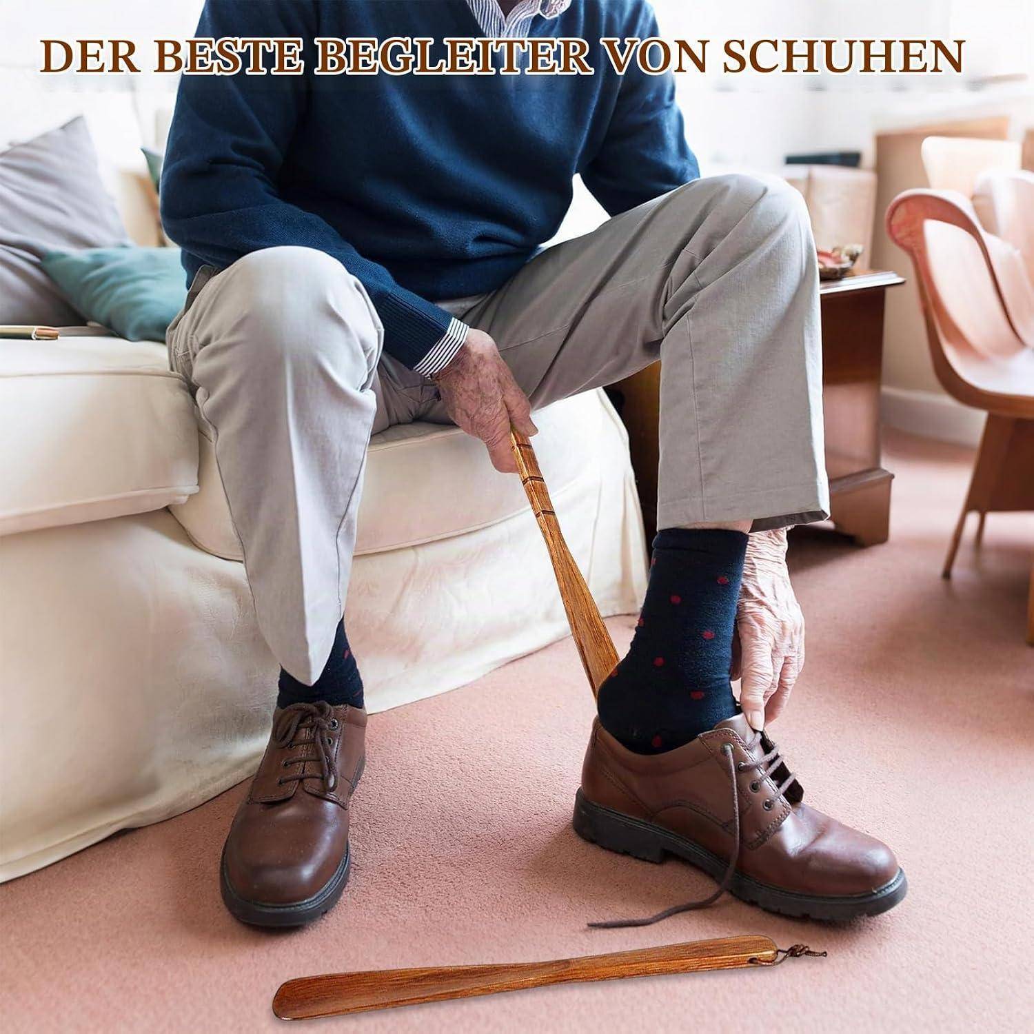 Ein älterer Mann sitzt auf einem Bett und benutzt einen Schuhanzieher mit langem Griff, um braune Lederschuhe anzuziehen; deutscher Text lautet „DER BESTE BEGLEITER VON SCHUHEN".