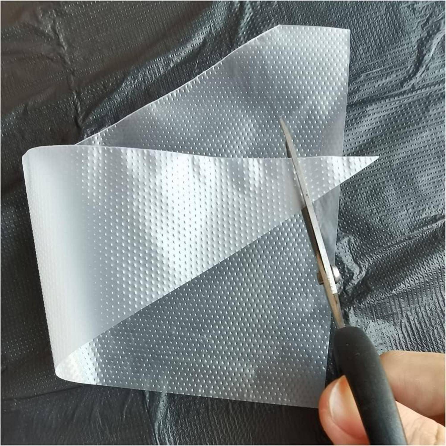 Mit einer Schere ein durchsichtiges gepunktetes Kunststoffblatt auf einer dunklen strukturierten Oberfläche von Hand zuschneiden.