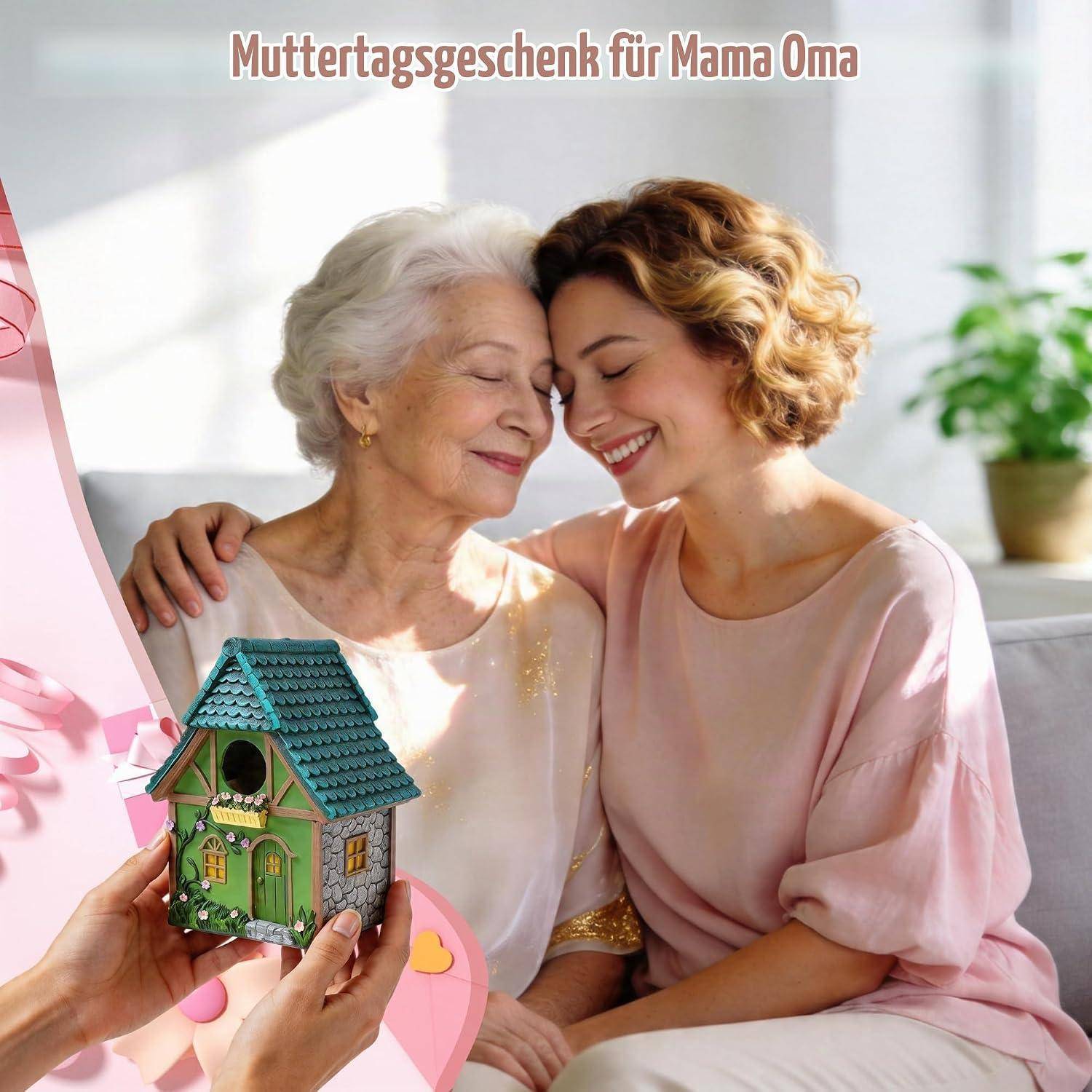 Junge Frau umarmt ihre lächelnde ältere Mutter, während sie ein kleines dekoratives Vogelhaus präsentiert; der Text lautet „Muttertagsgeschenk für Mama Oma