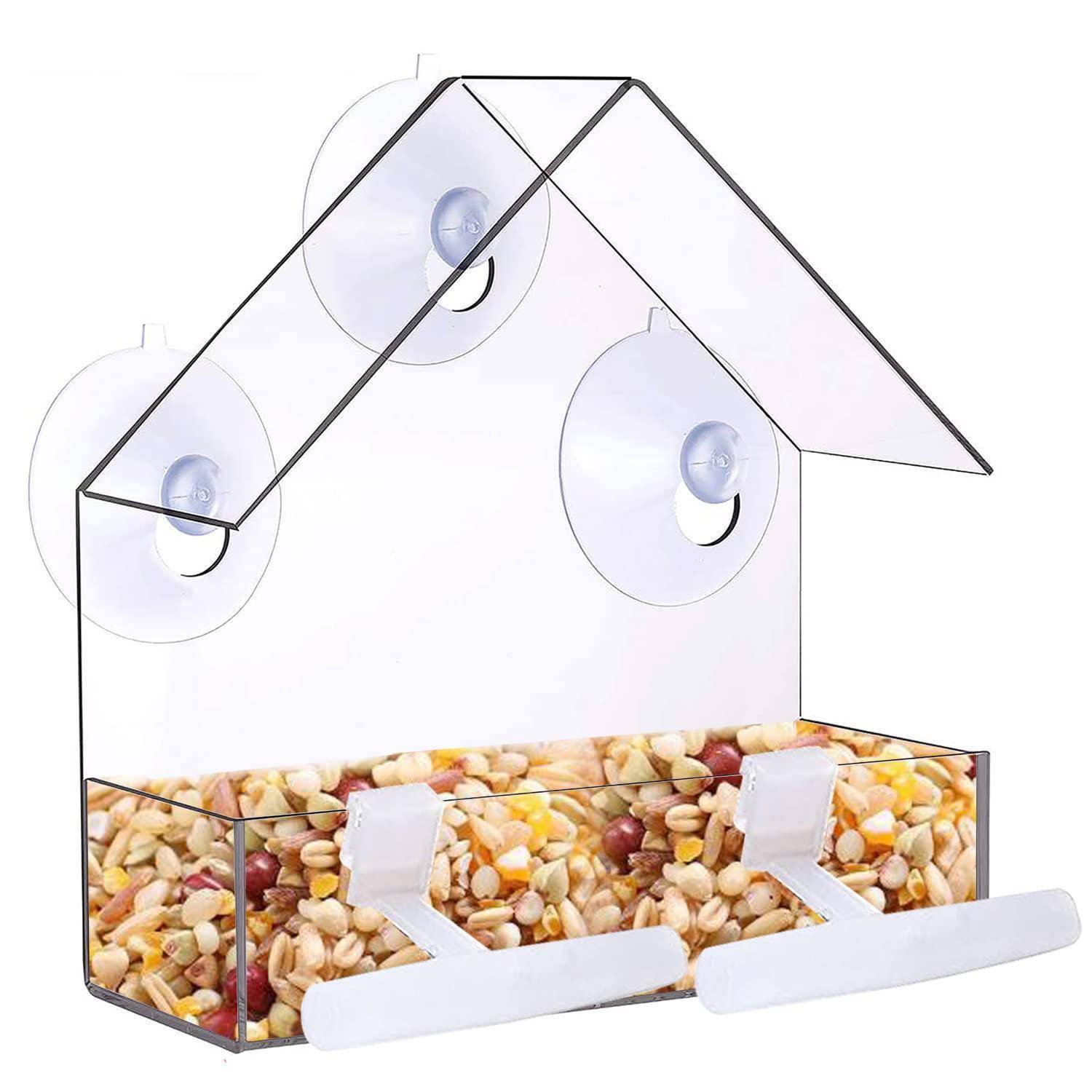 Klarer Acryl-Wandmontage-Vogelfutterhaus mit zwei Saugnäpfen, einem spitz zulaufenden Dach und einer Samenschale gefüllt mit gemischtem Vogelfutter.