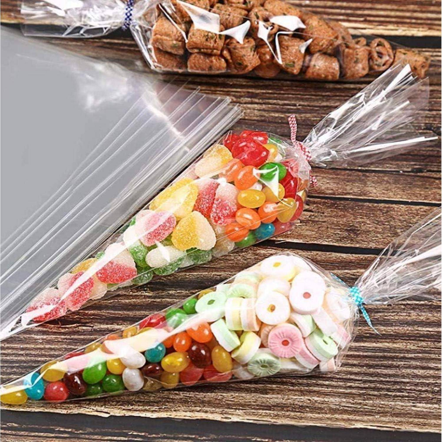 Durchsichtige, kegelförmige Plastiktüten gefüllt mit verschiedenfarbigen Bonbons und Gummibärchen auf einer Holzoberfläche, mit einer verschlossenen Tüte mit Schokoladenbissen im Hintergrund.
