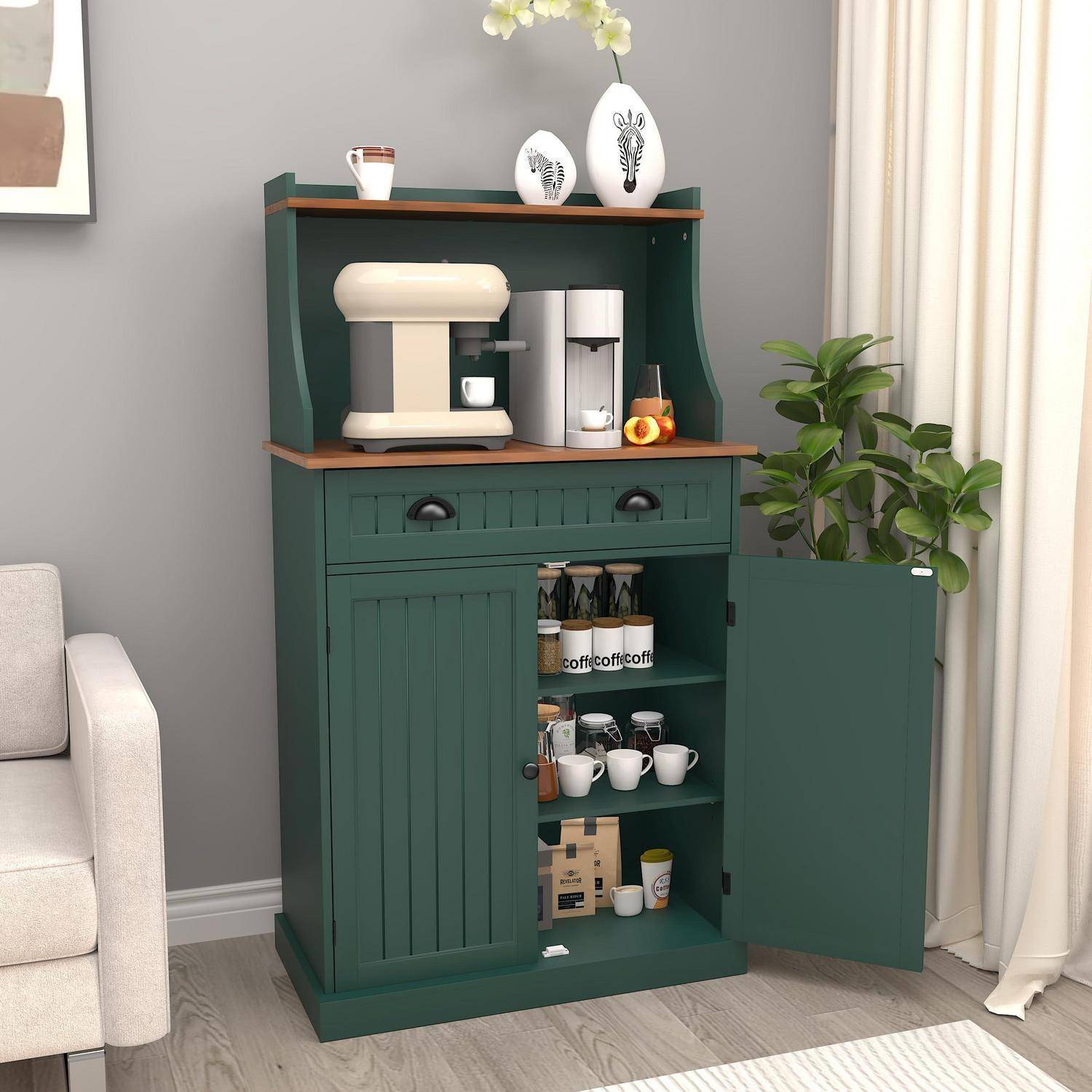 Grüner Küchenschrank mit offener Kaffeestation, Espressomaschine und Tassen, plus eine Topfpflanze neben einem Sofa in einem hellen Wohnzimmer.