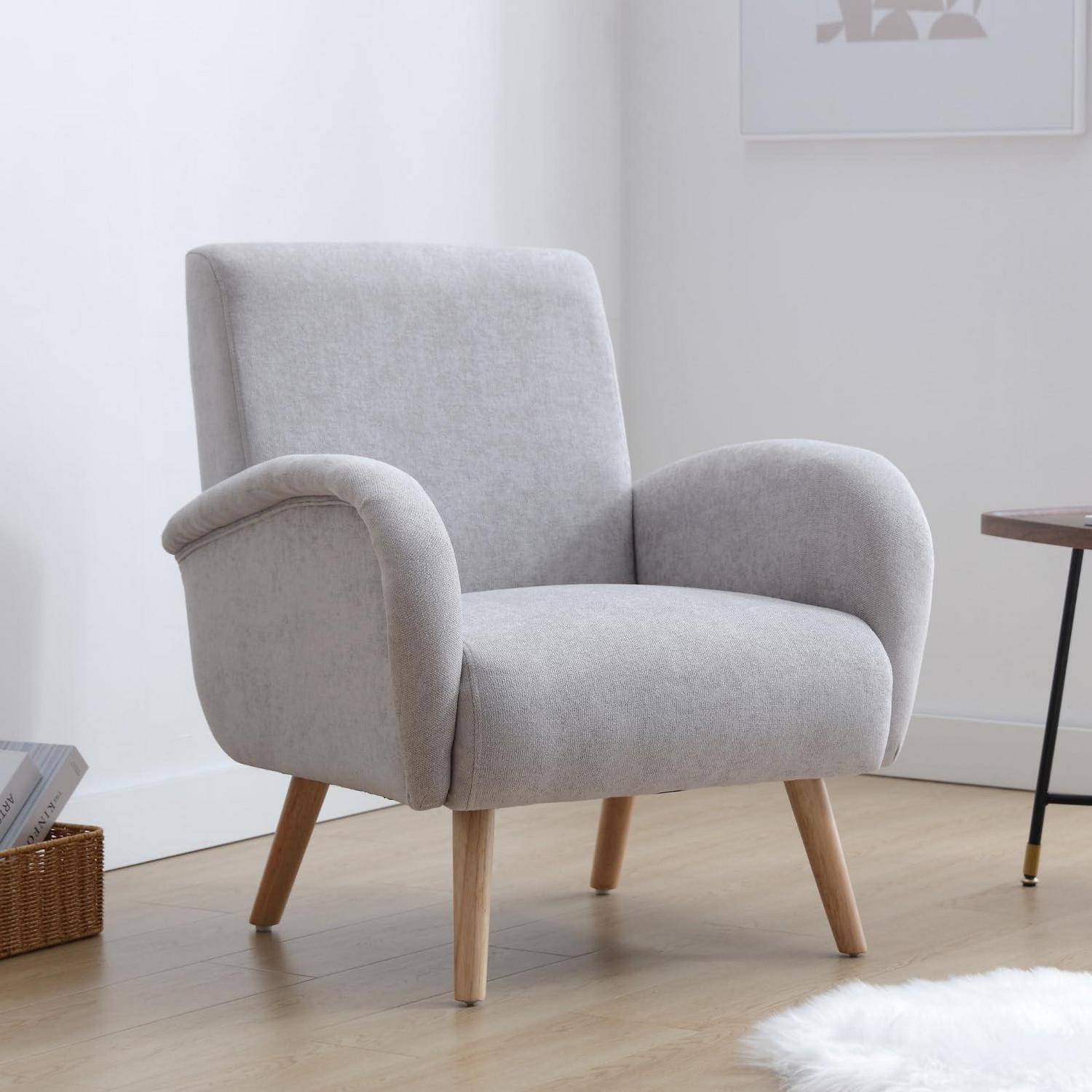 Hellgrauer gepolsterter Sessel mit Holzbeinen in einem minimalistischen Raum neben einem kleinen Tisch.