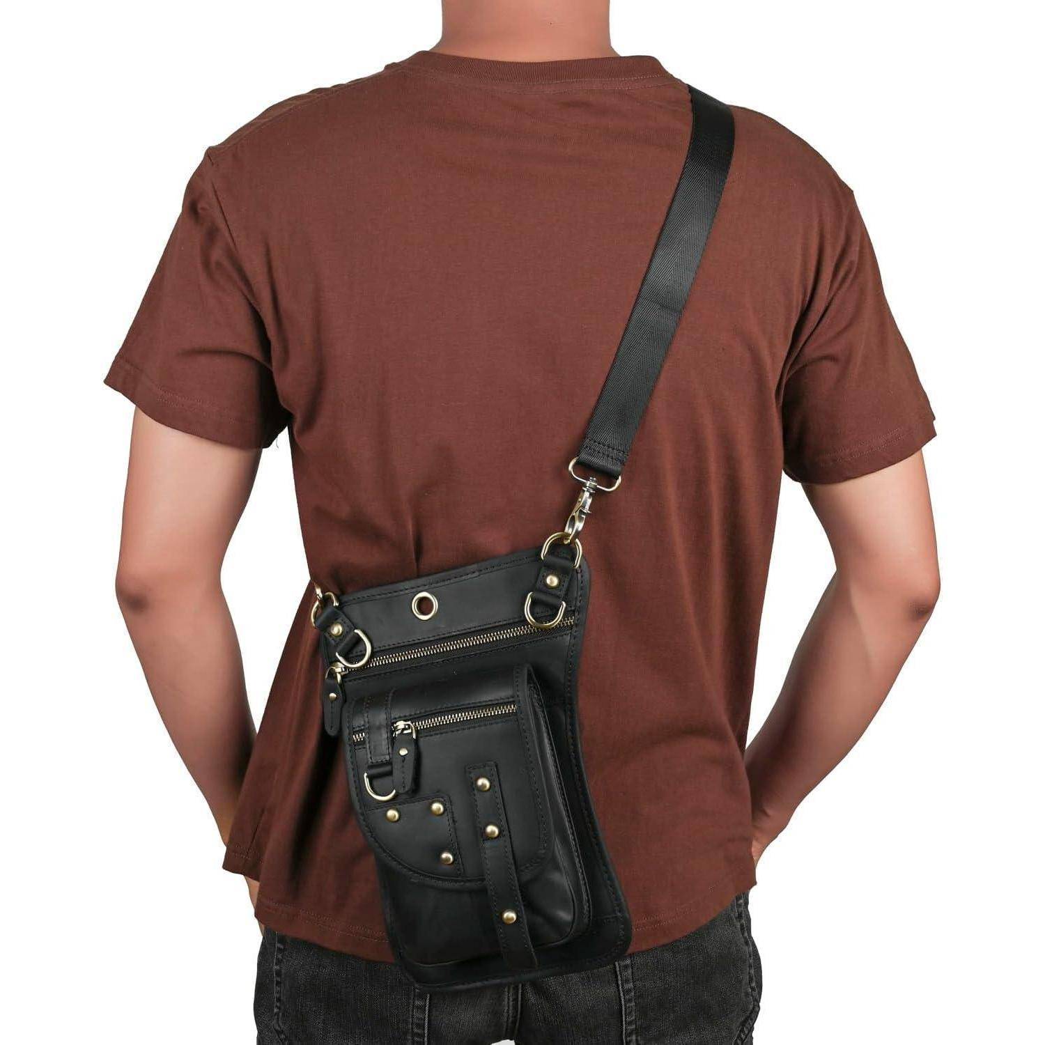 Rückansicht einer Person, die eine schwarze Umhängetasche mit mehreren Reißverschlusstaschen und Metallnieten über einem braunen T-Shirt trägt.